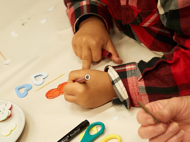 A child's hand colours in surrounded by craft supplies