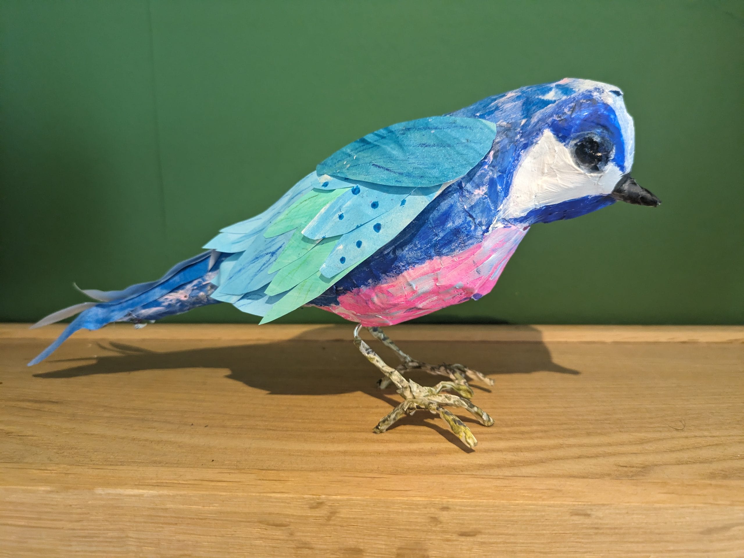 A small blue and green bird, with a pink breast created out of paper