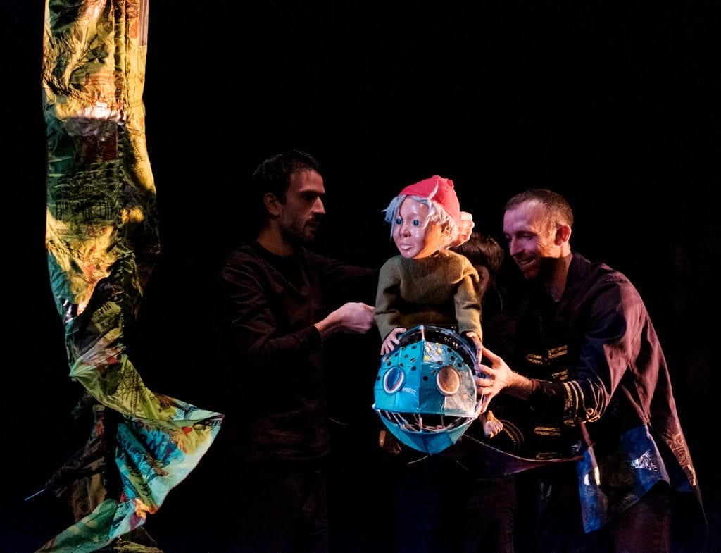 two mwn in dark setting holding a sculpture of a water sprite.