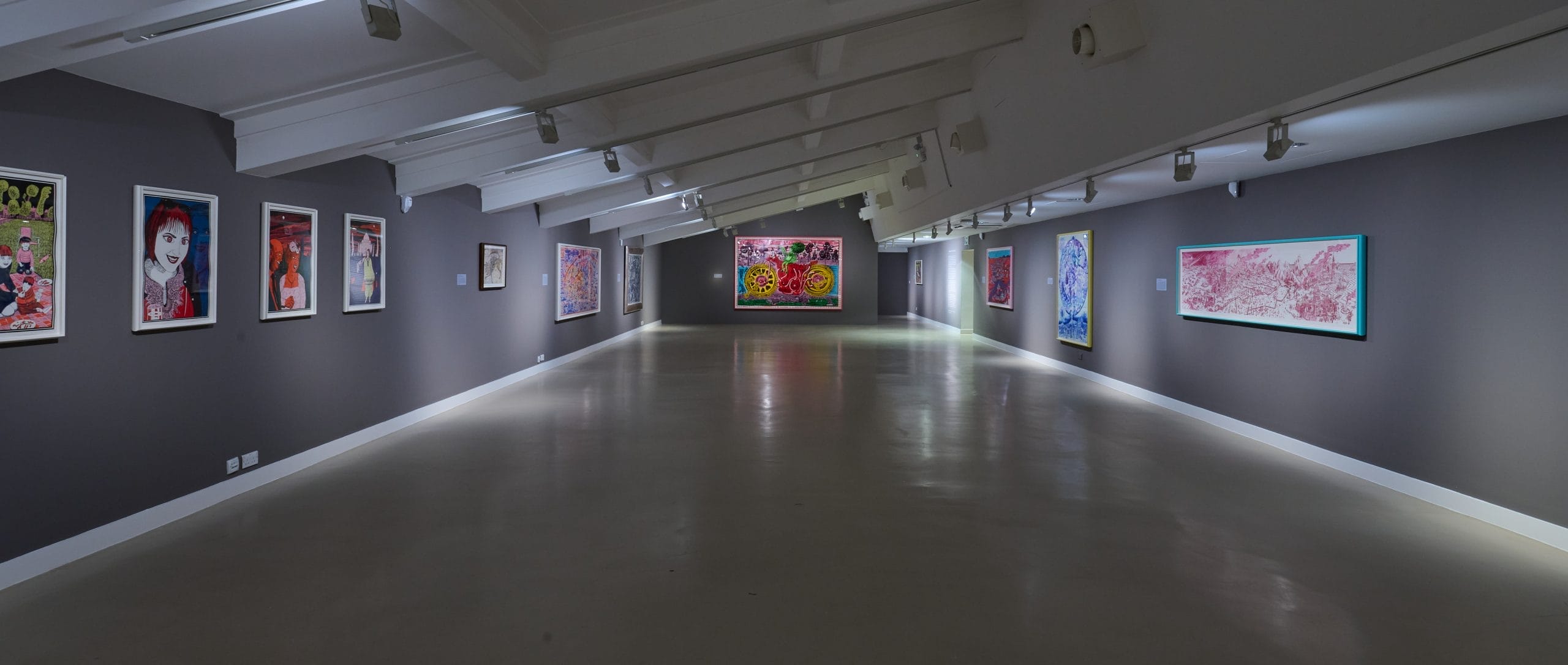 A long grey gallery space featuring brightly colour prints by artist Grayson Perry, on all three walls.