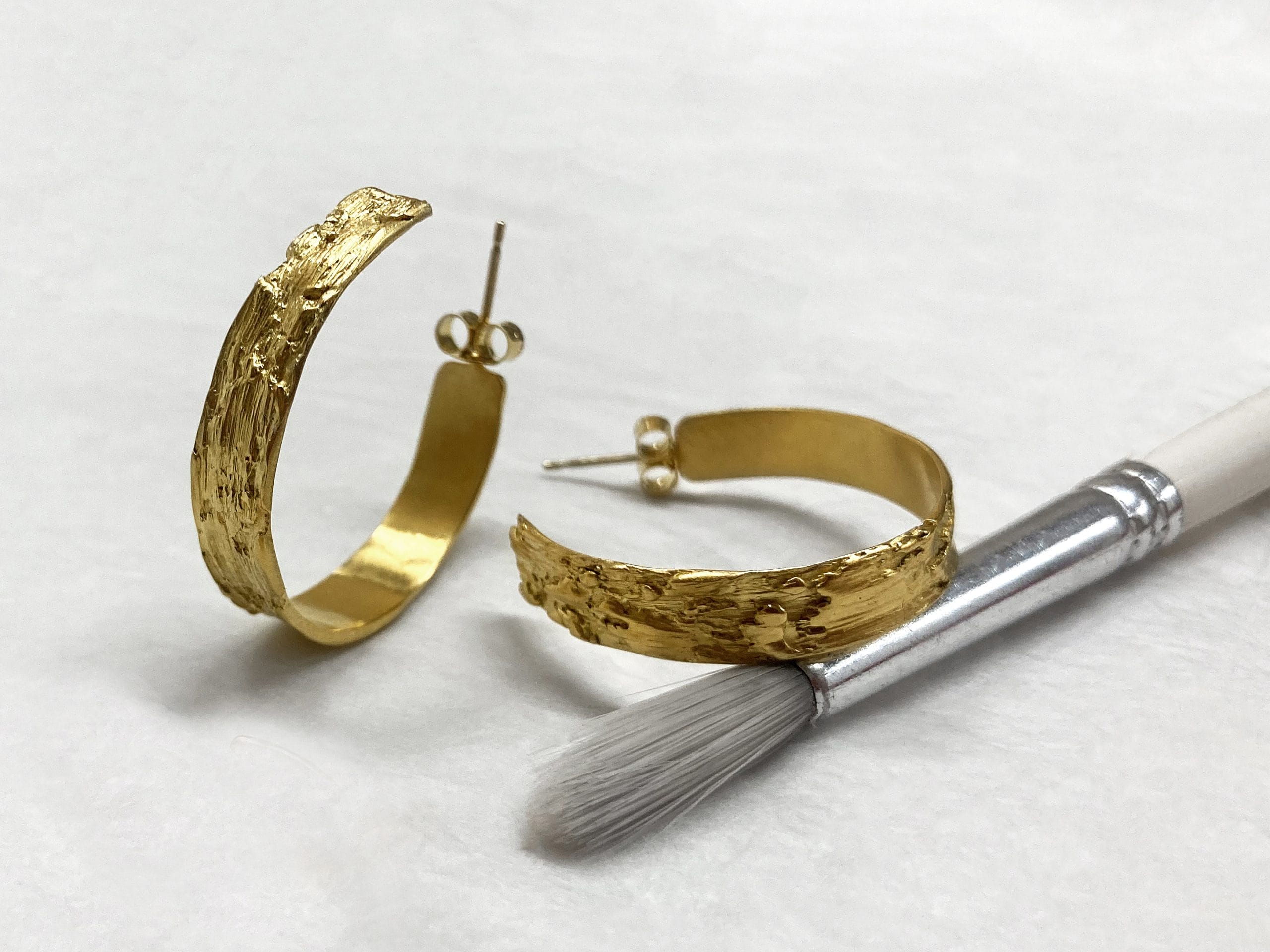 a pair of gold hoop earrings next to a small brush