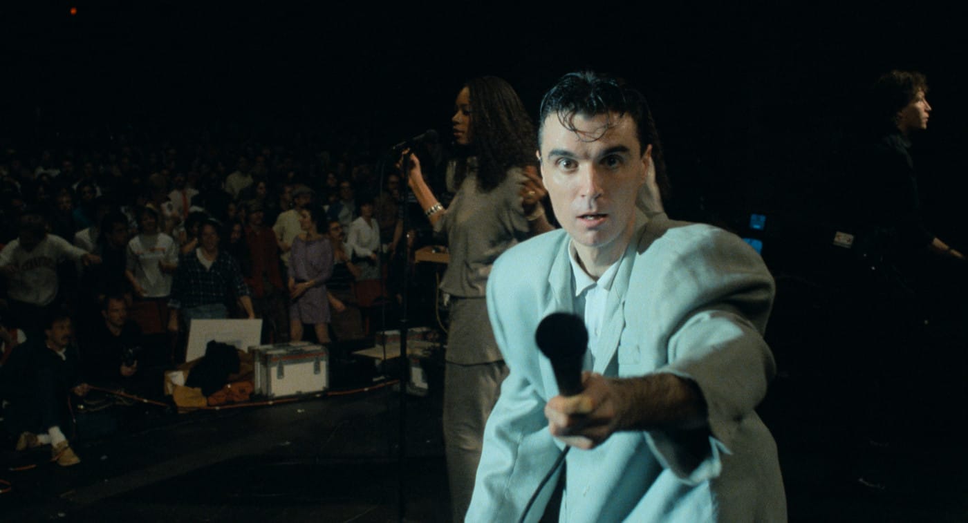 David Byrne holding a microphone towards the camera