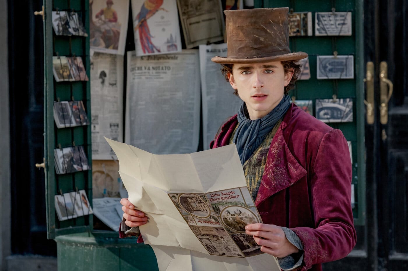 Willy Wonka (Timothée Chalamet) dressed in a burgundy jacket and brown top hat.