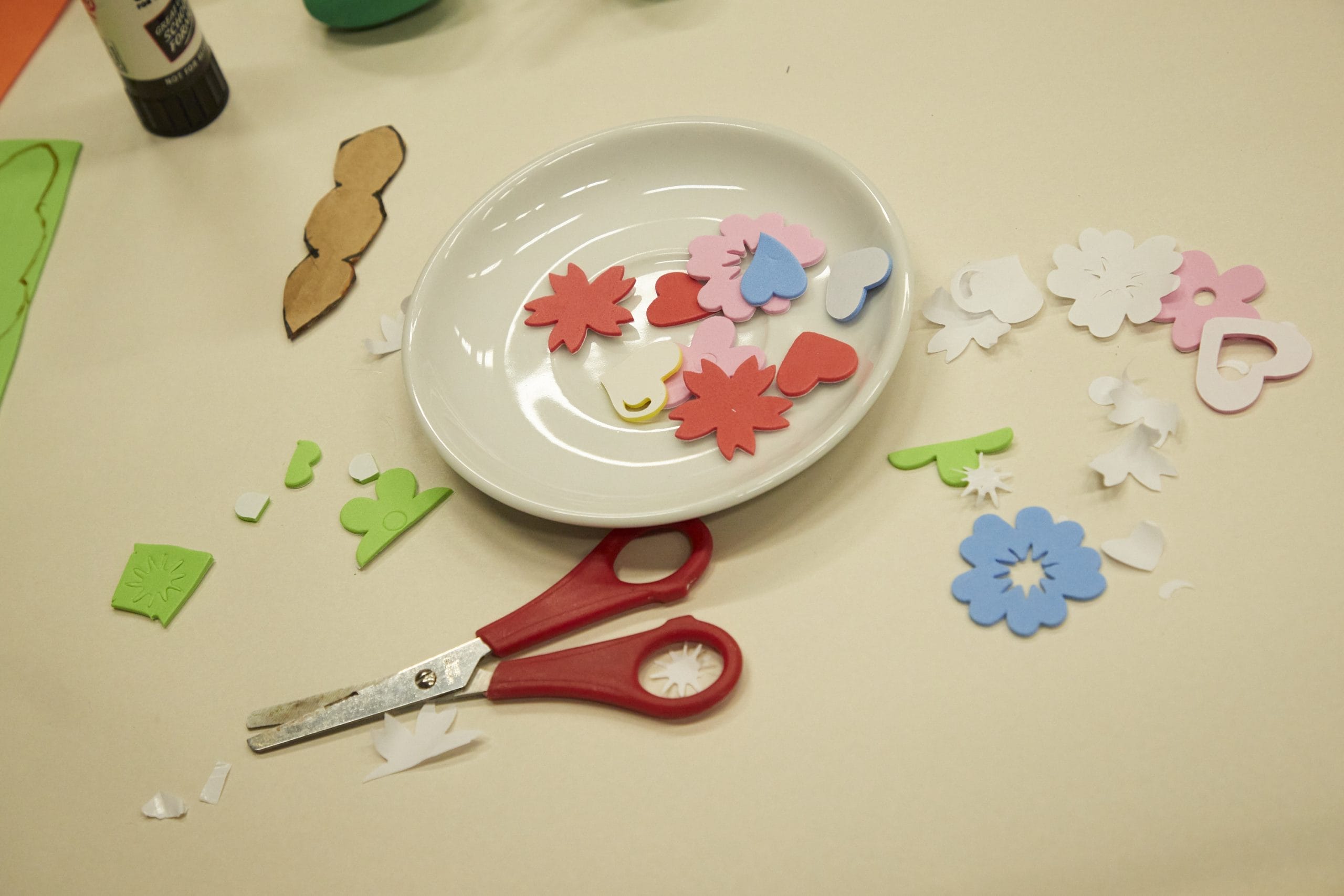 A dish on a table with a pair of scissors and various shapes cut out in brightly coloured paper.