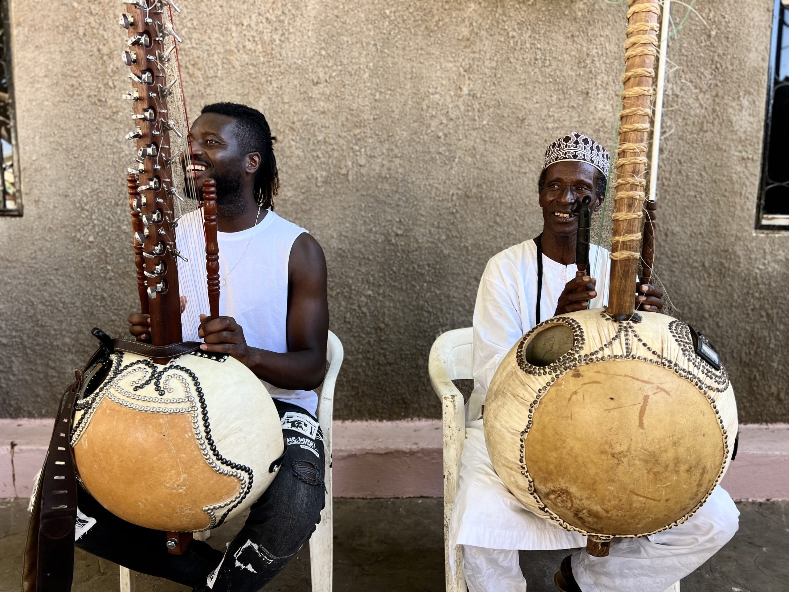 Two African men sit on chairs holding Koras, traditional instruments.