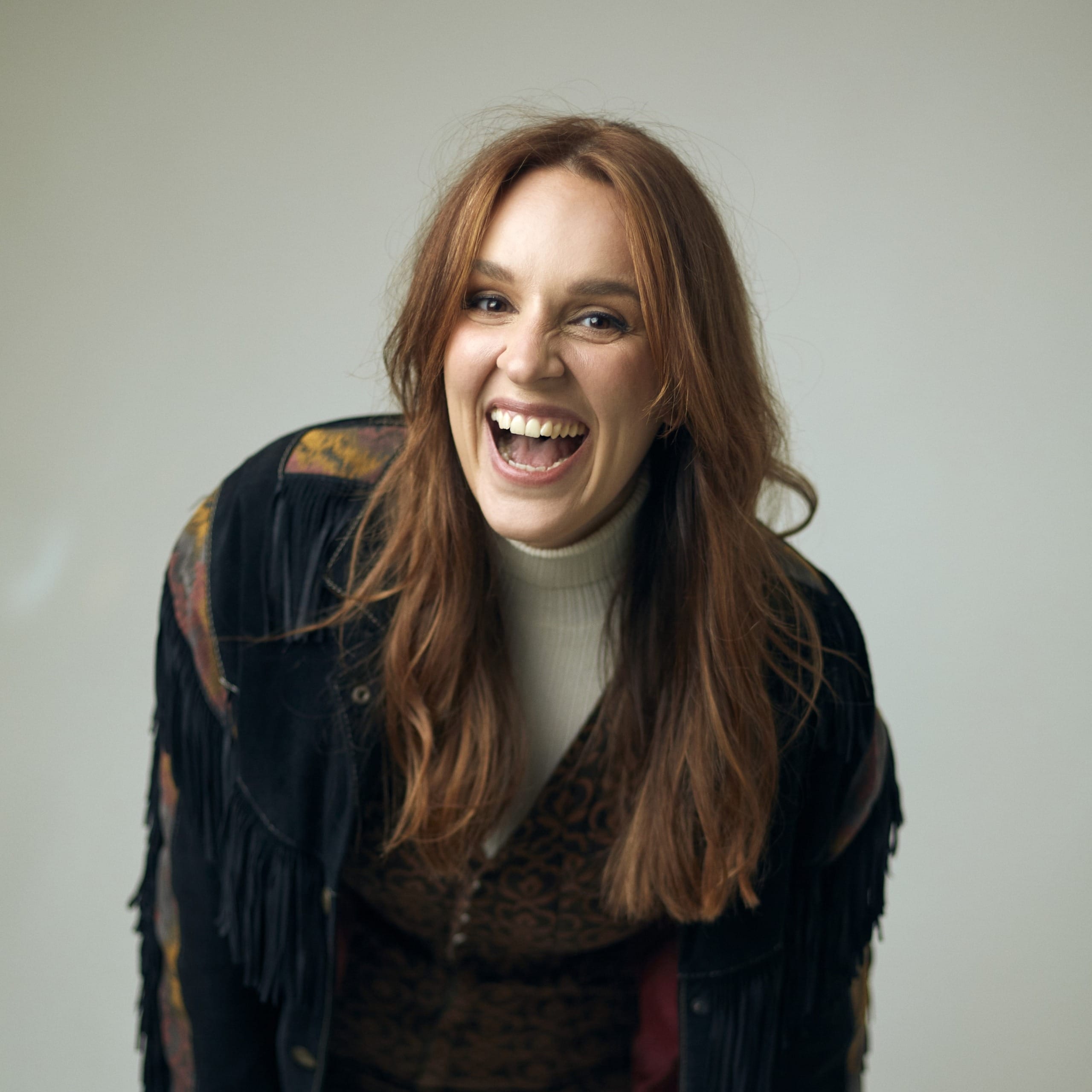 A woman with long auburn hair smiles towards the camera.