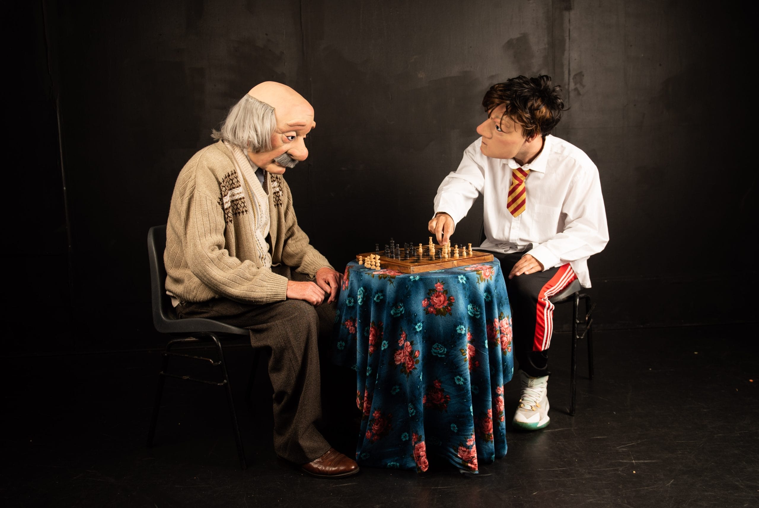 A photo of a boy and an old man wearing masks on a stage playing chess