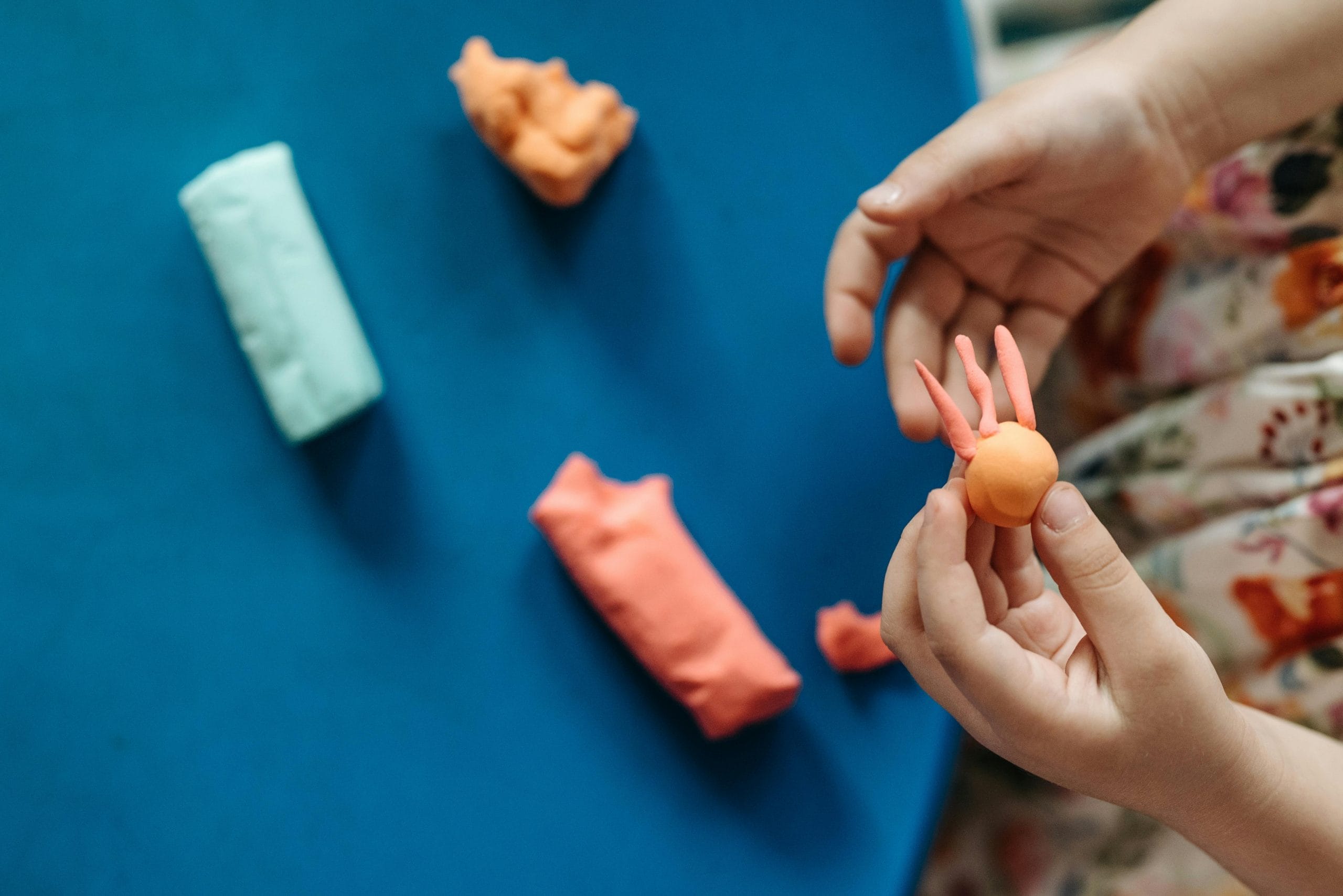 Small hands playing with clay on a blue table