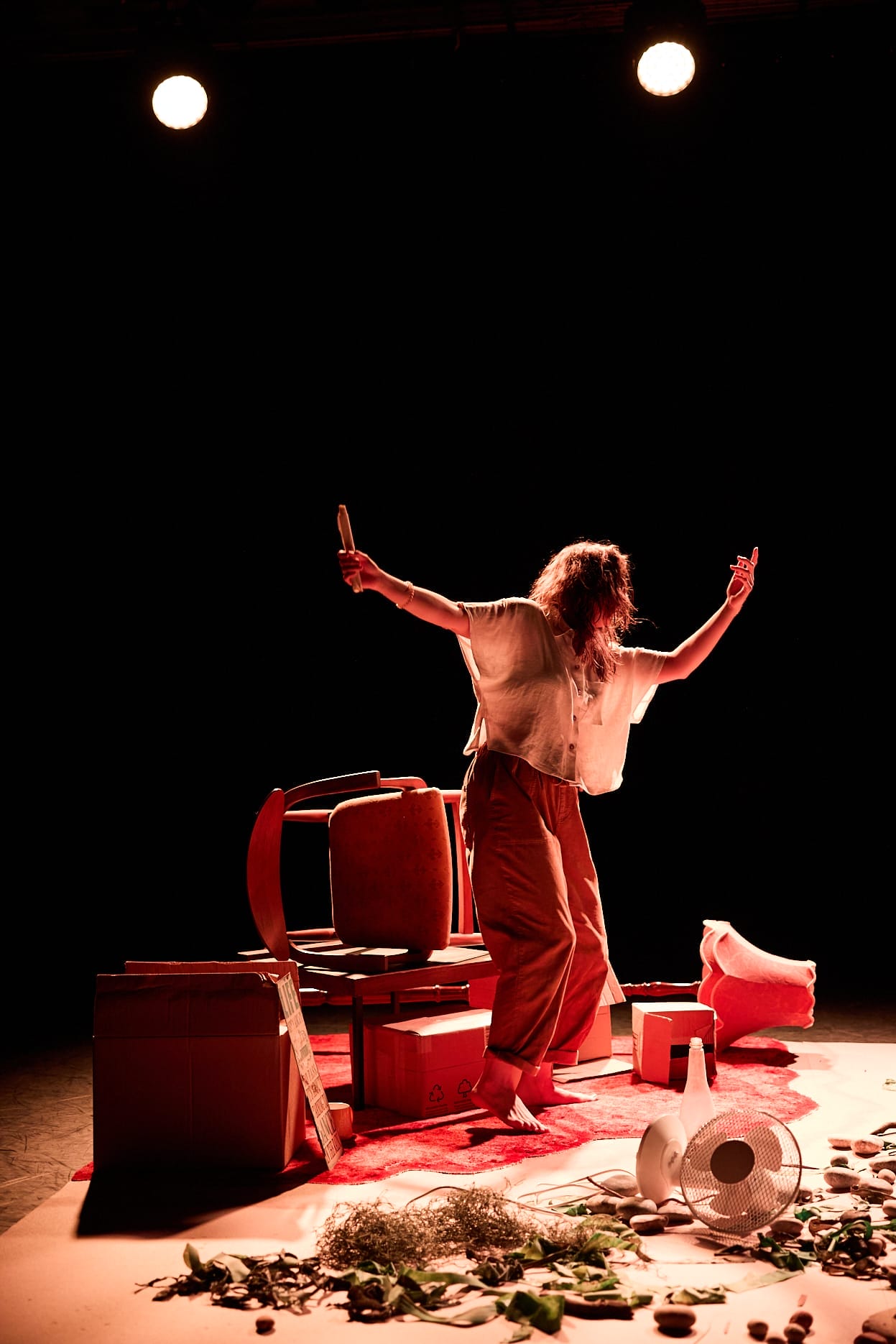 a woman on stage surrounded by living room set with a broken plant pot in the front on the floor
