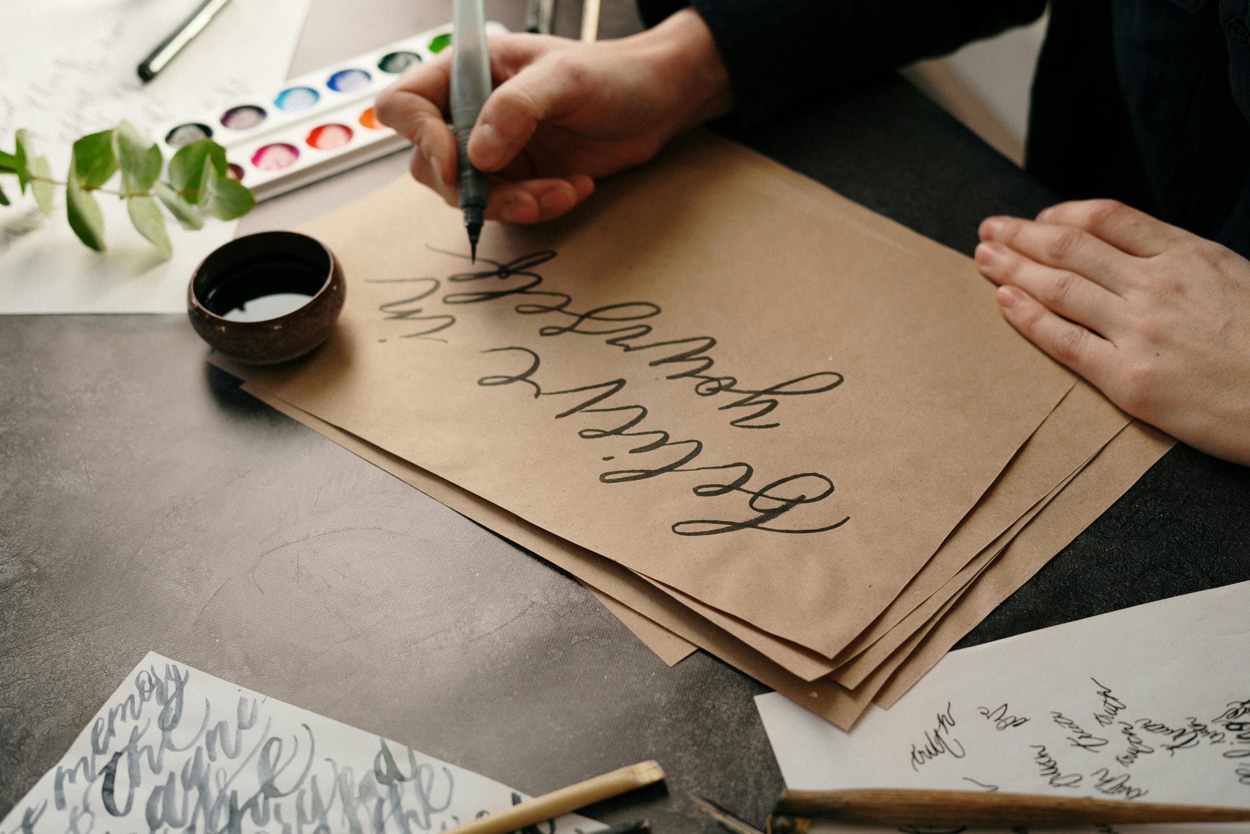 A hand holding an ink pen writes on brown paper.