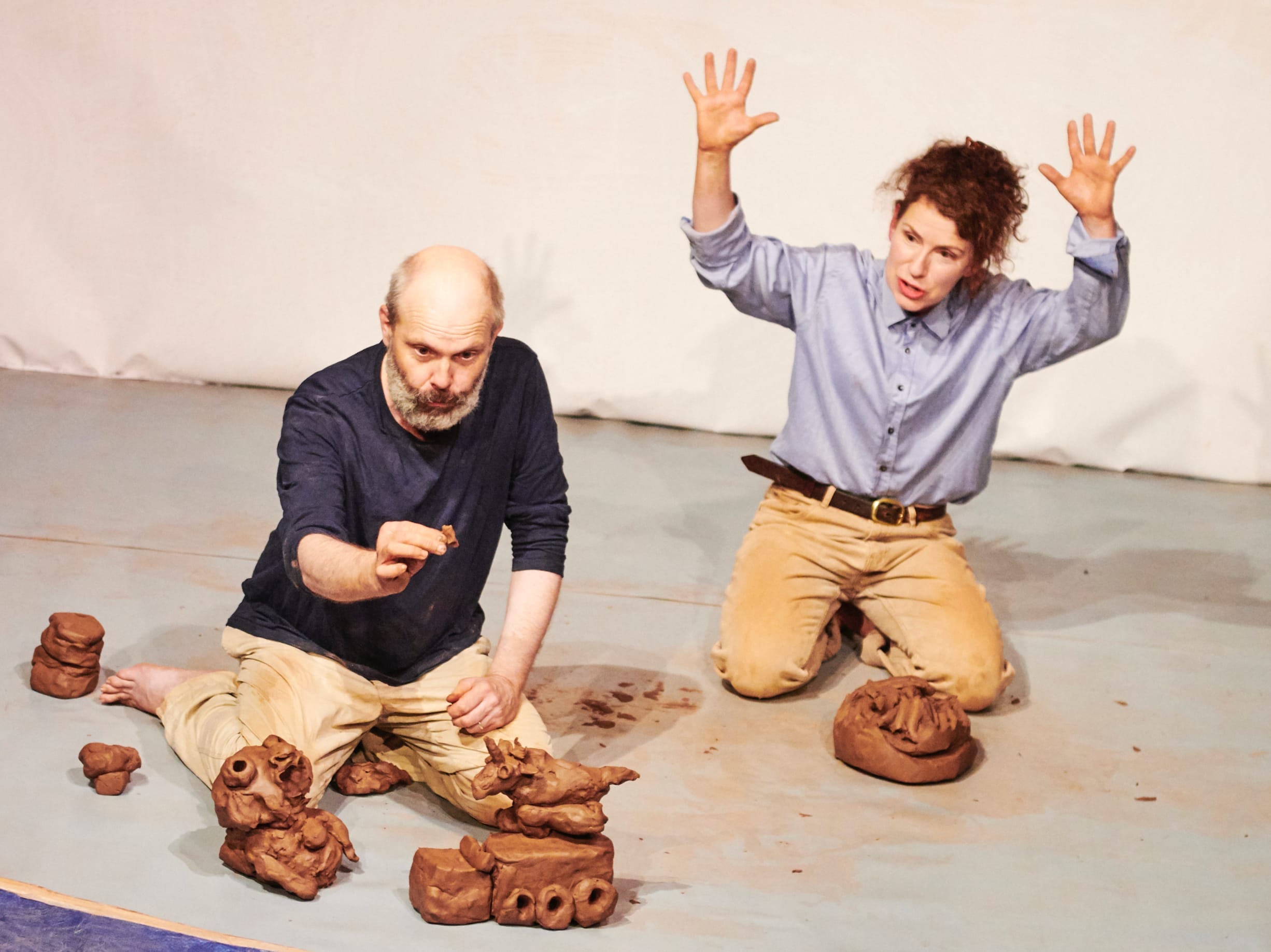 a woman and a man are kneeling on a stage where they built vehicles and creatures out of clay