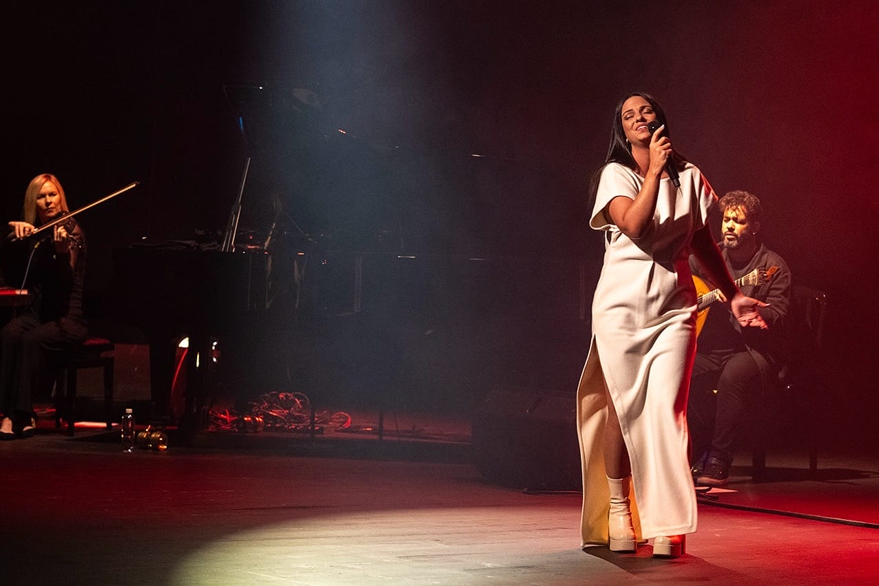 Fado Singer Lina_ performing on stage in a white dress with two other musicians in the background