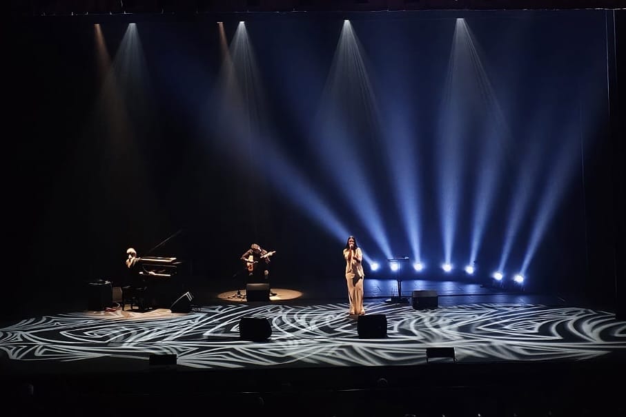 Fado Singer Lina_ singing on a stage with lights around her and musicians in the background