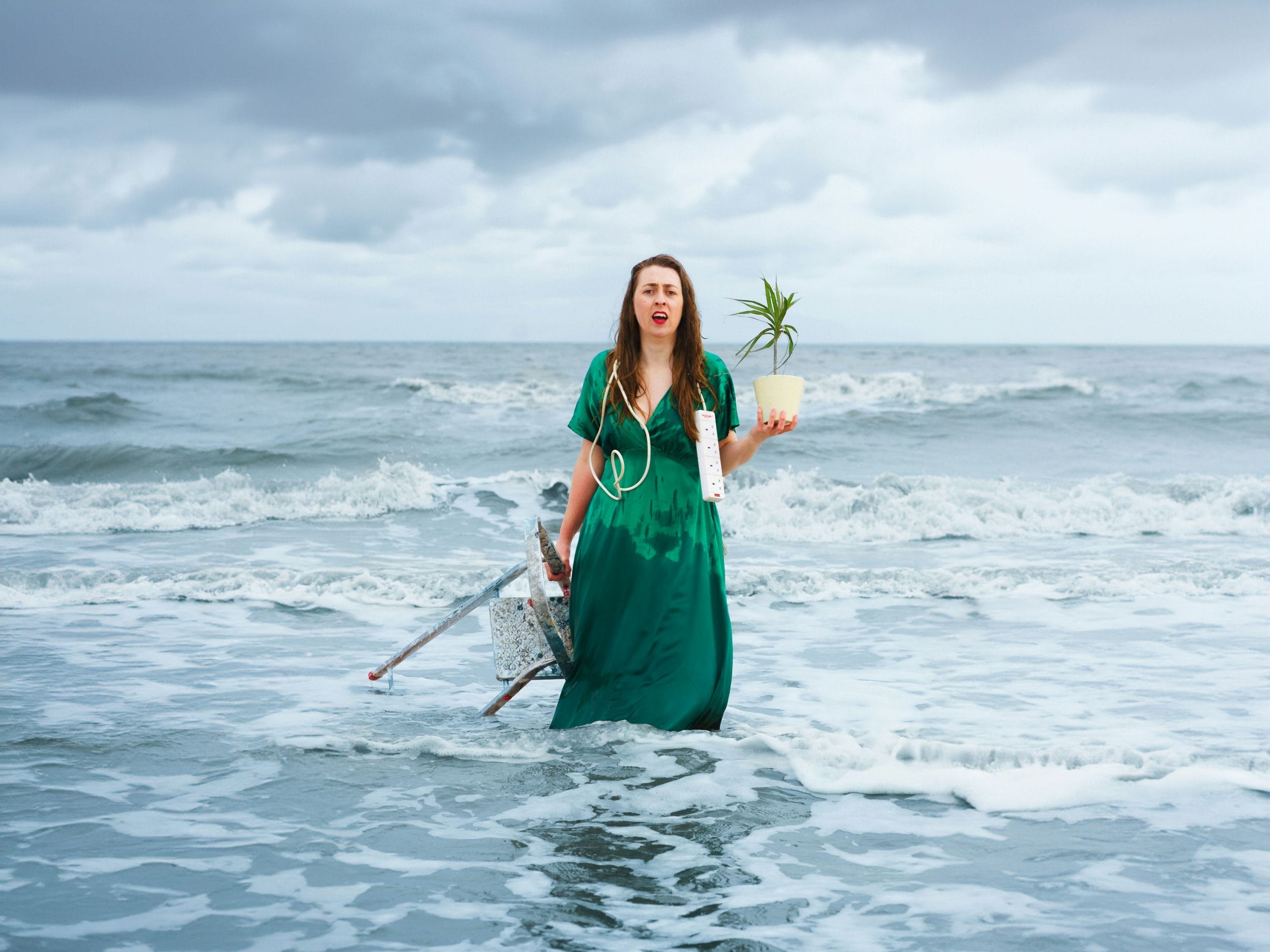 Woman standing in the sea holding a plant pot and step ladder