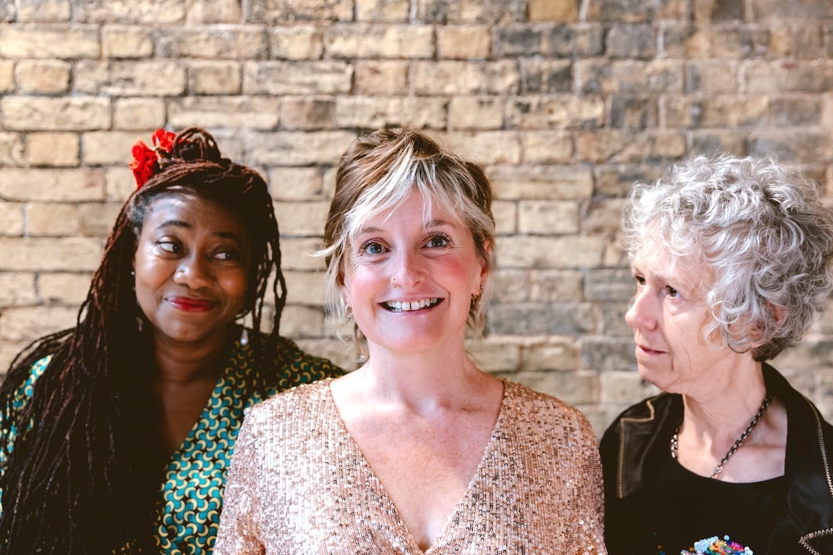 Three women stand in front of a brick wall.