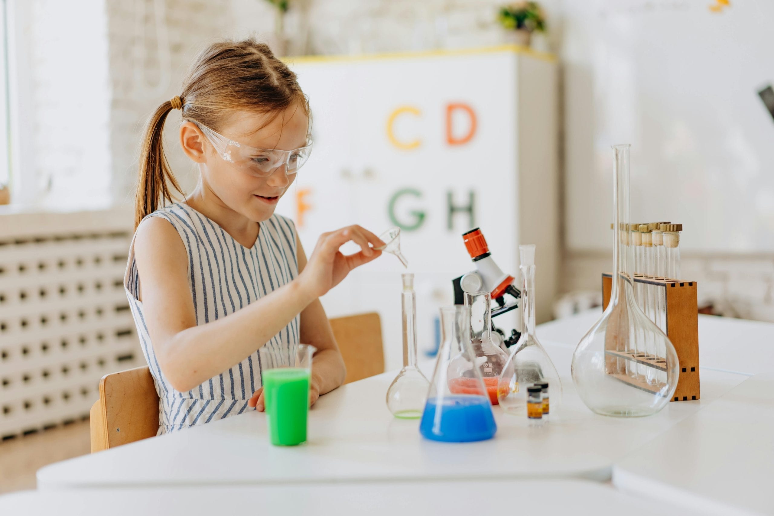 A small girl with pigtails sits at a table conducting a science experiment.