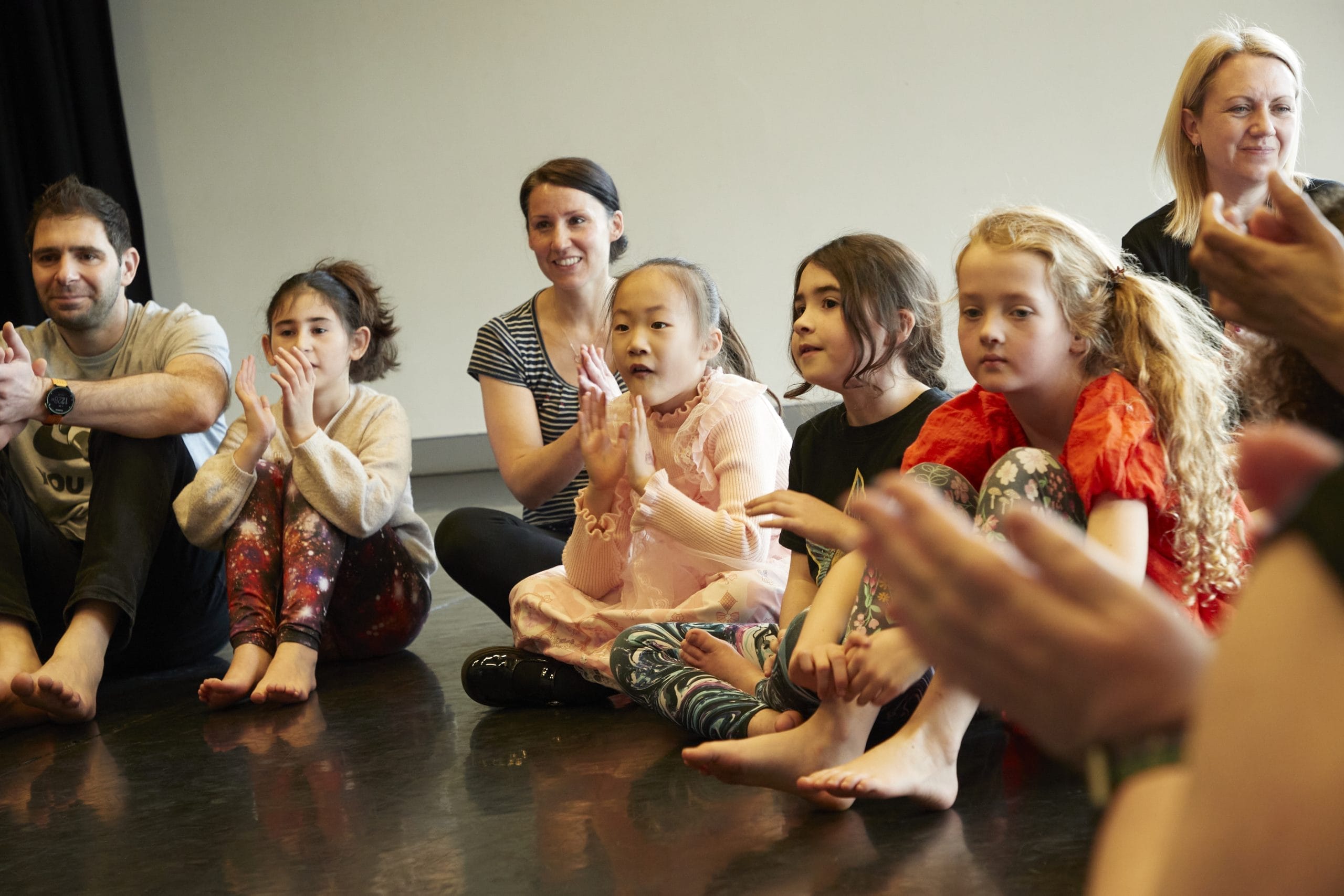 A group of animated children sit on a dark floor listening to a story.