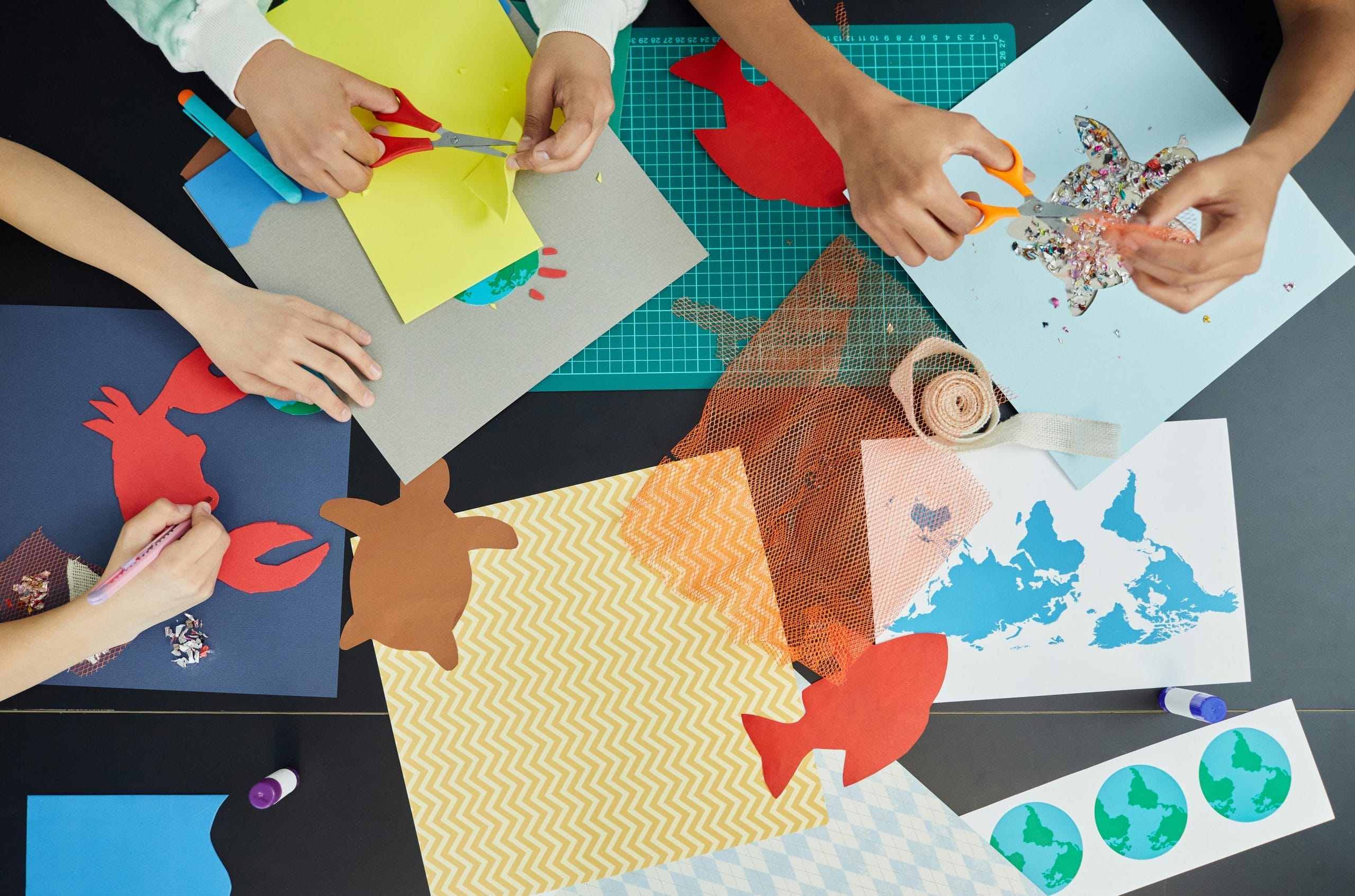 A table full of craft supplies with children's hands cutting and sticking.