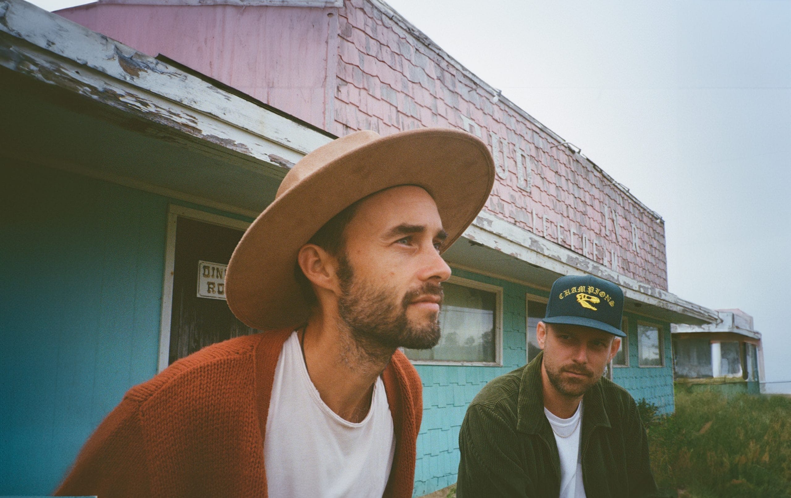 Two young men wearing hats sat in front of turquoise garages.