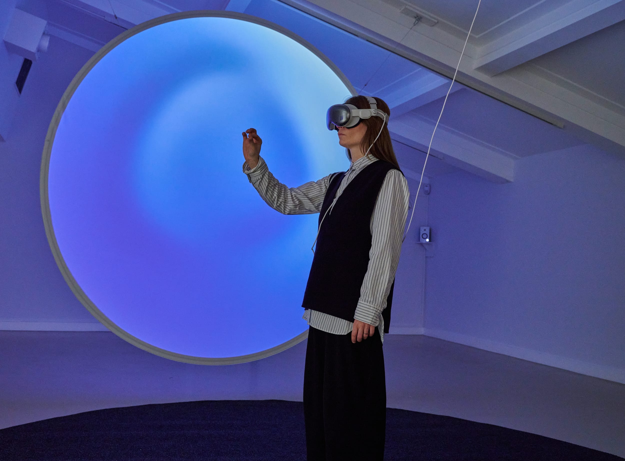 A person, wearing VR googles stands in front of a circular blue screen.