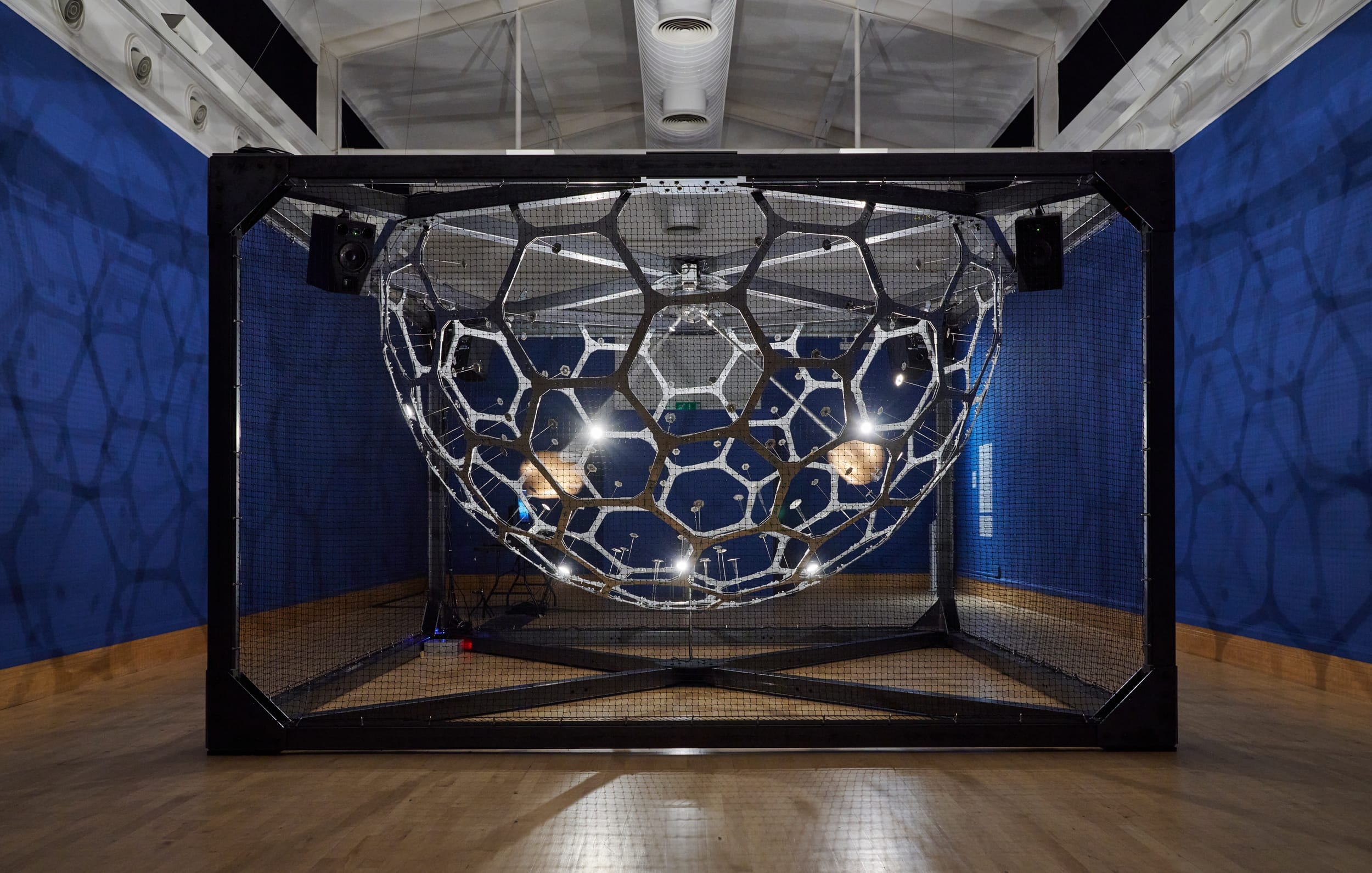 A metal spherical cage sits in a metal frame, two brass bells rotate inside.