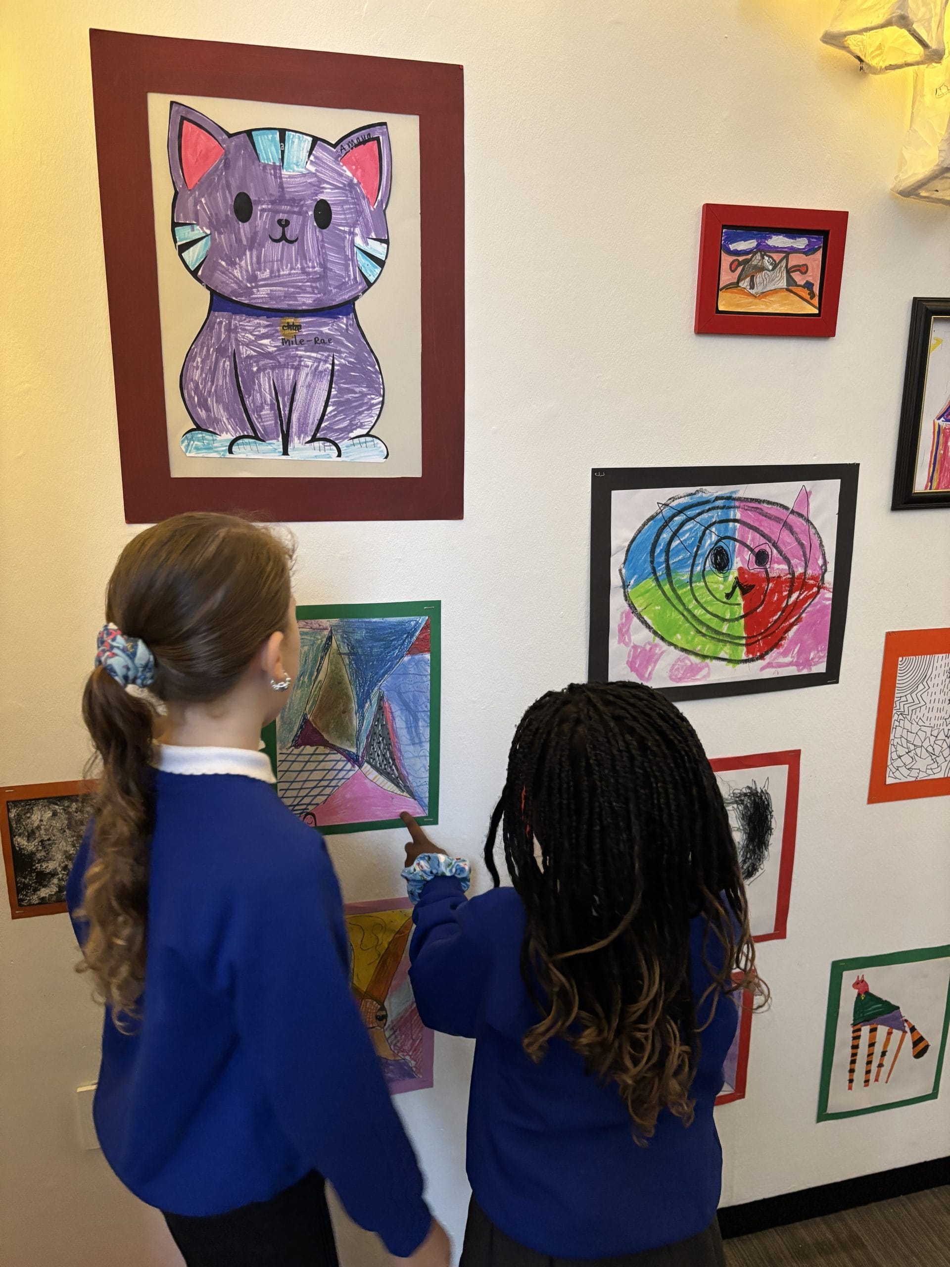 two schoolchildren looking at drawings of cats create by their classmates