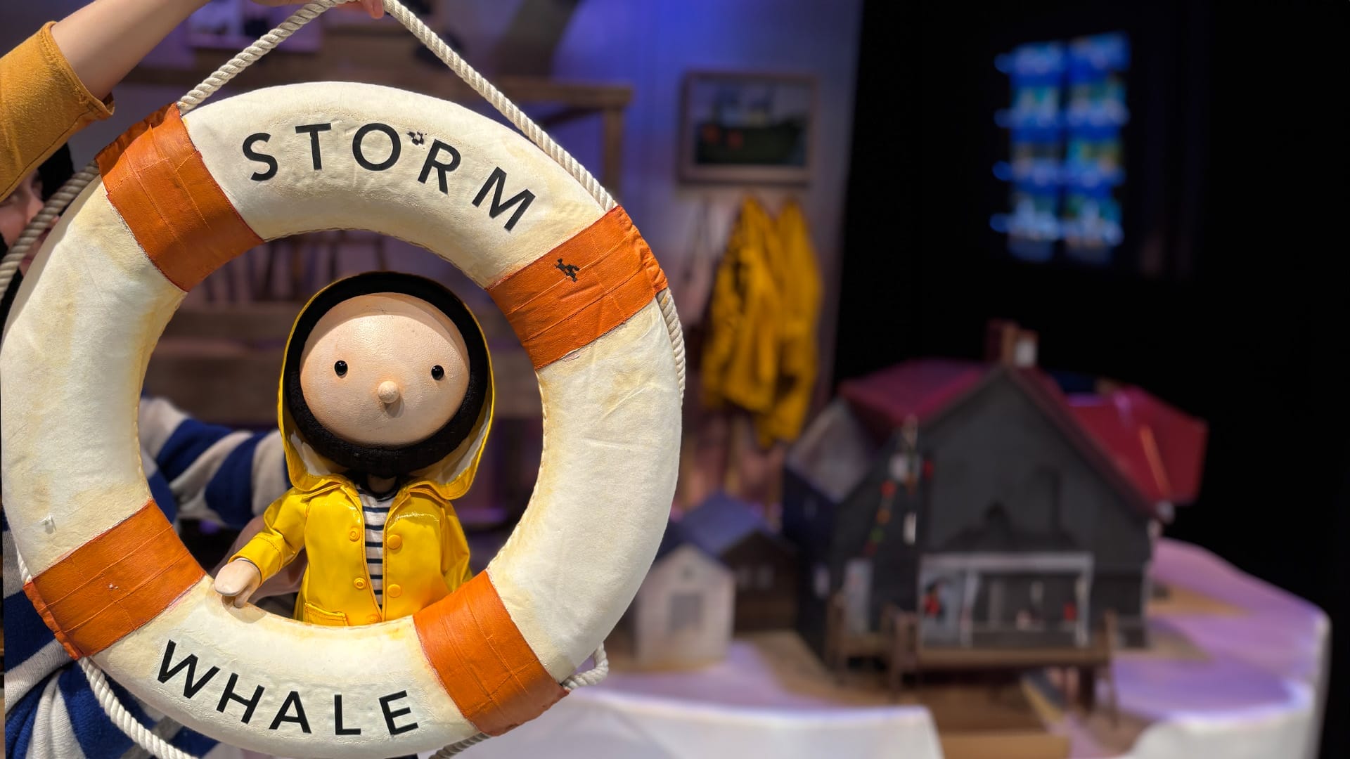 A small puppet in a yellow coat, peeps through a lifeboat ring.