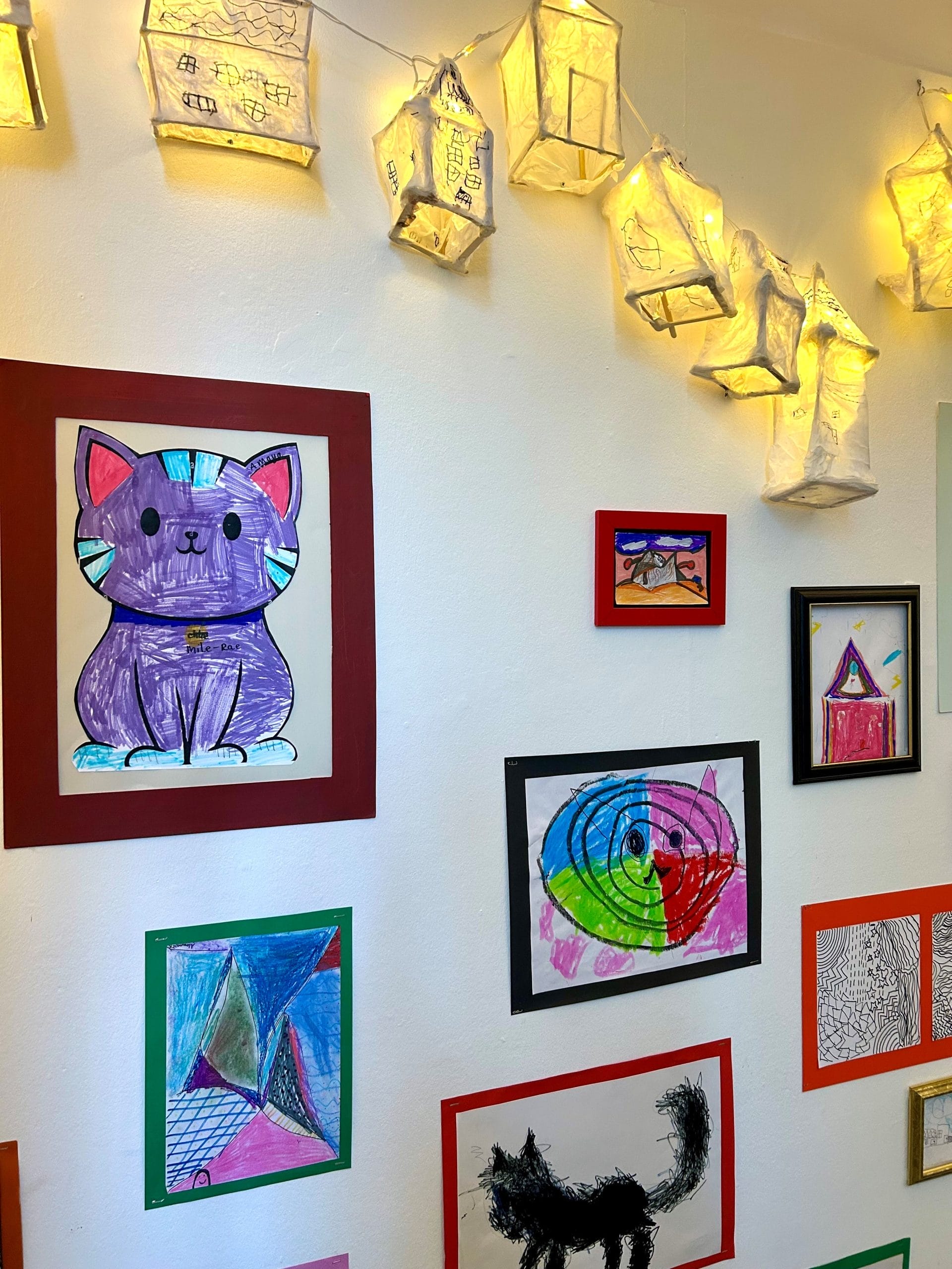 lots of drawings of cats by schoolchildren displayed on a white wall