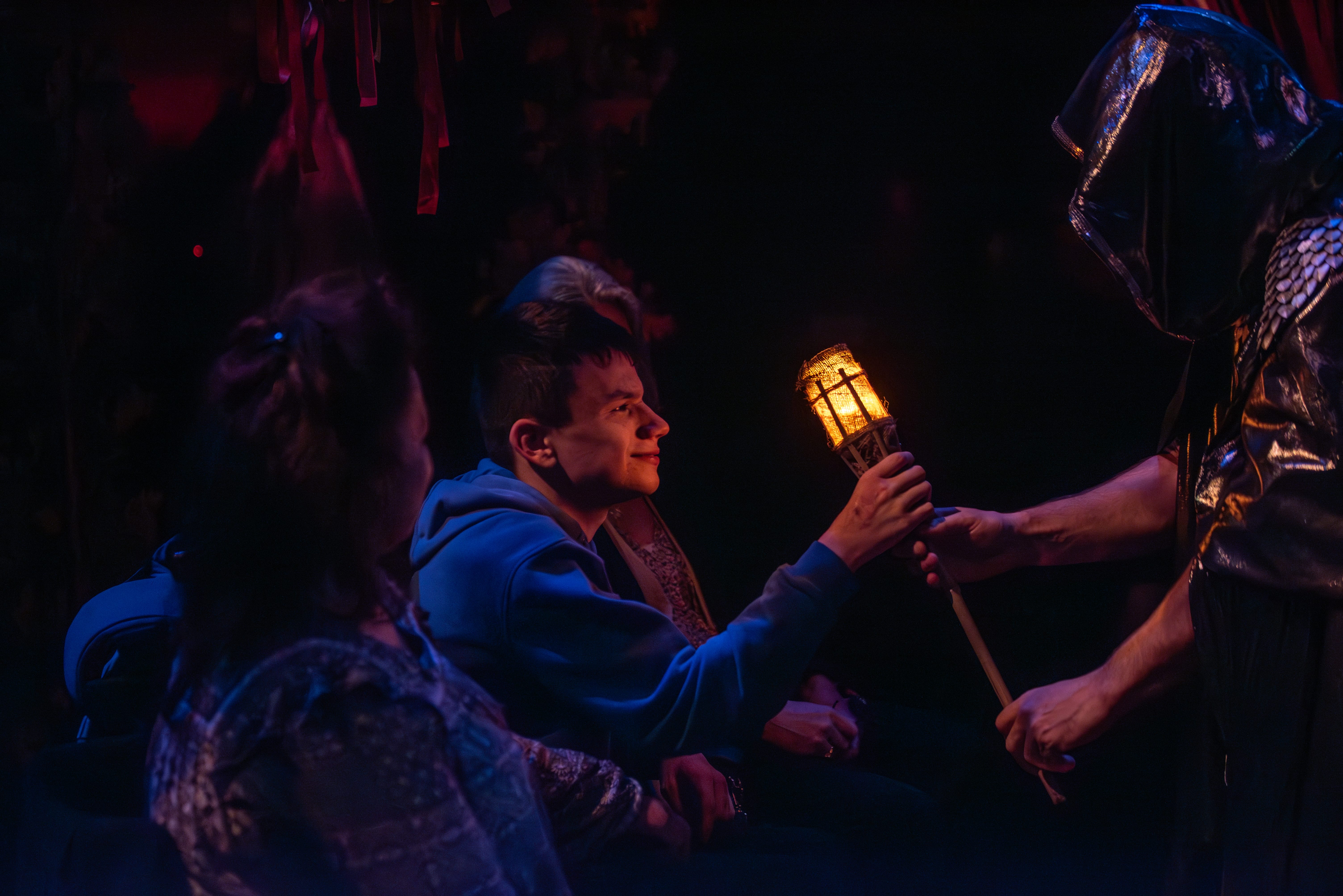 An audience member dressed in a blue jumper touches a torch held by an actor