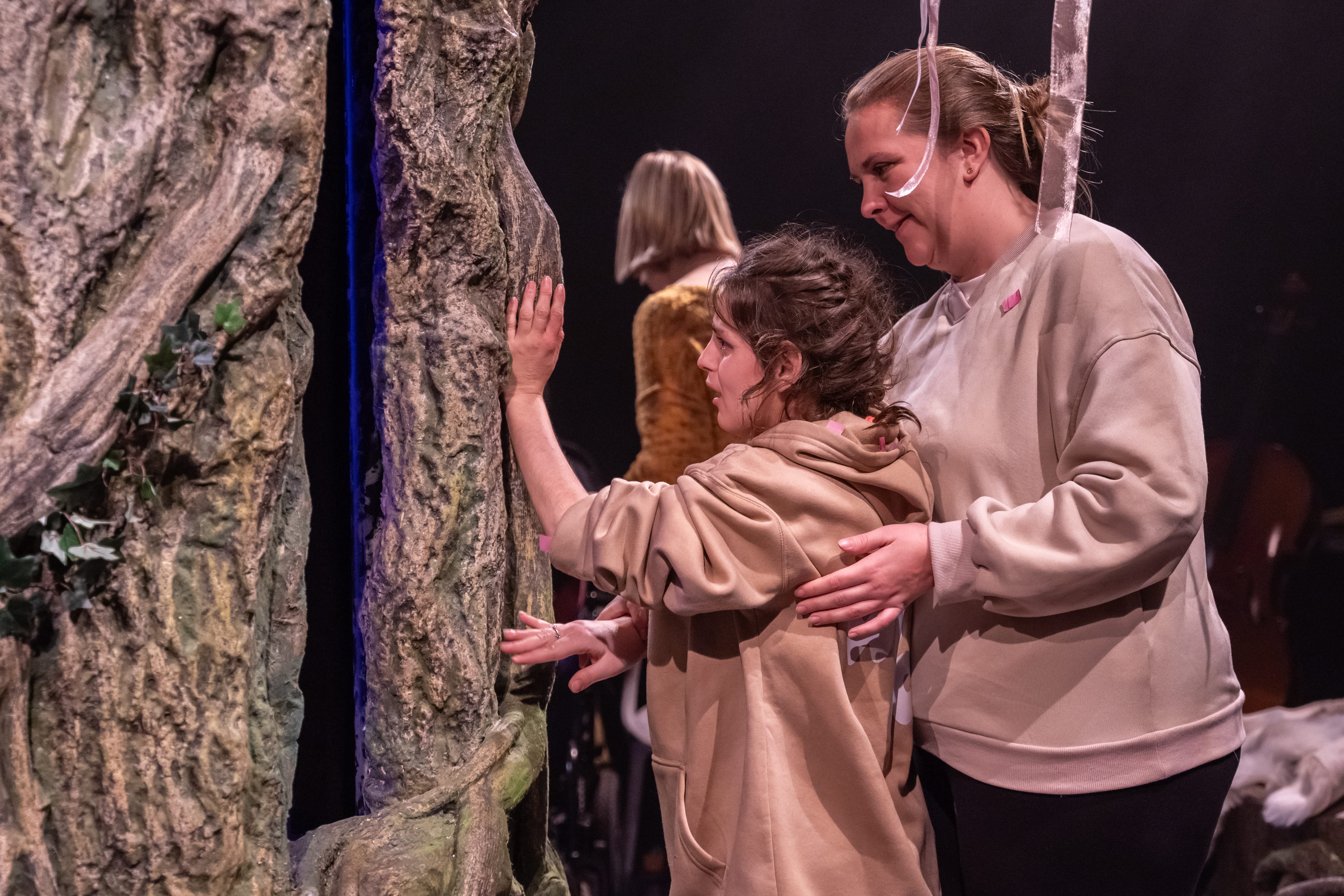 An audience member touches a tree on the set while supported by their carer