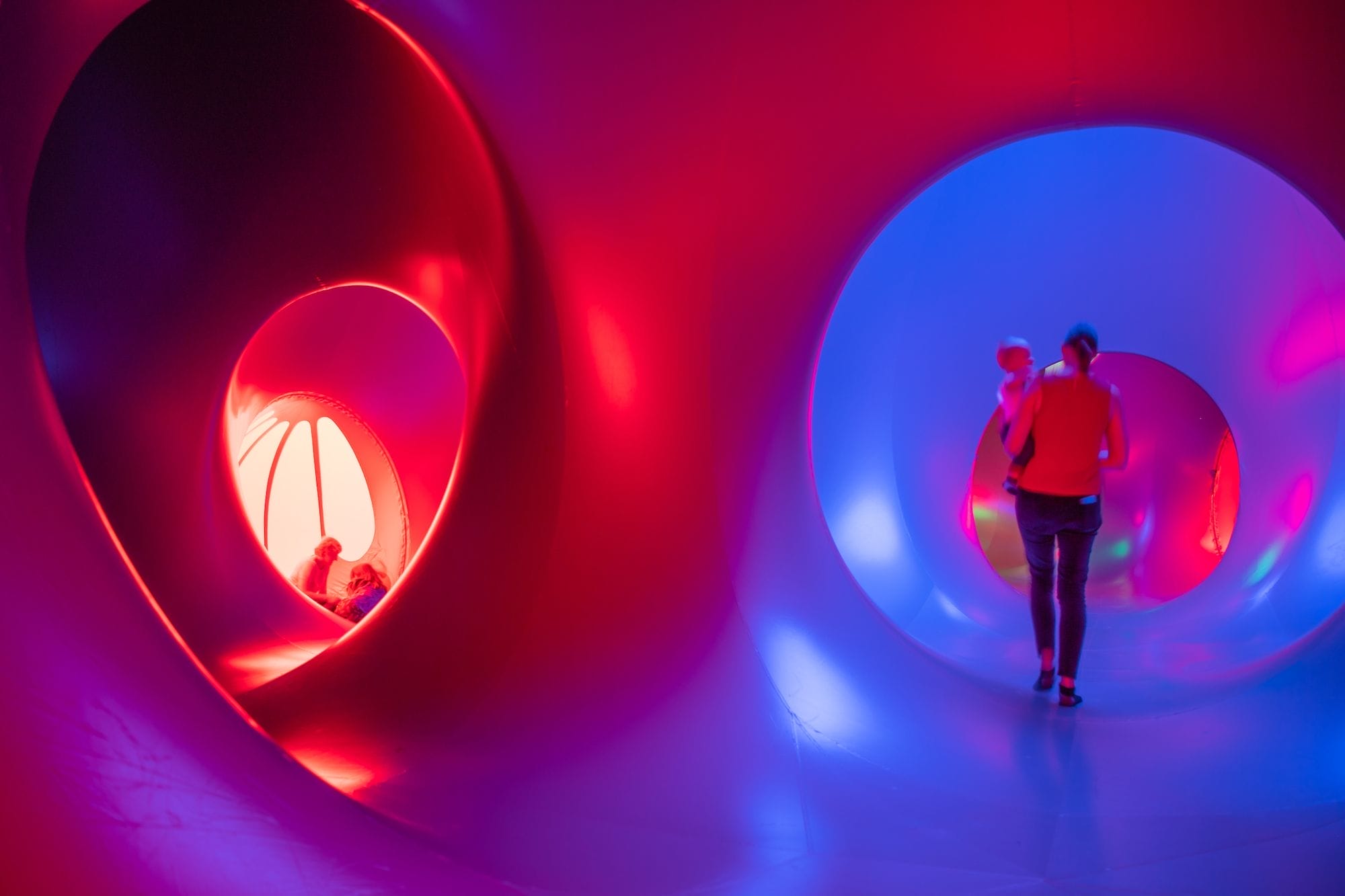 internal photo of a luminarium with visitors walking through it and enjoying it sitting on the floor