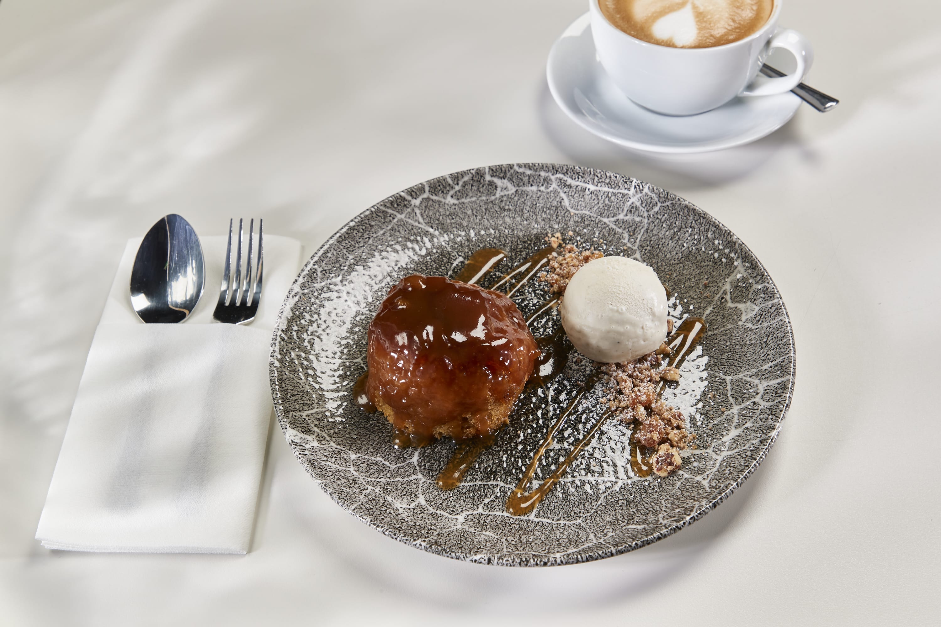 A silver plate holds a sticky toffee pudding with toffee sauce and vanilla ice cream.