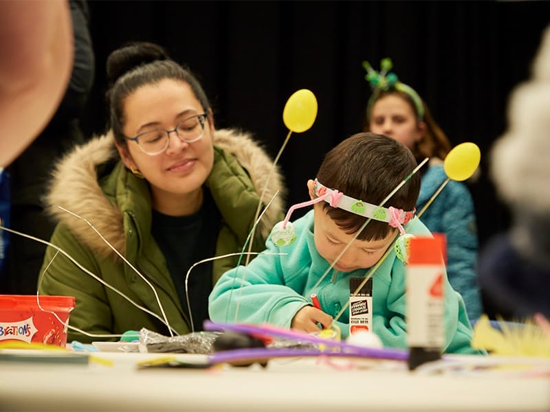 A woman and small boy concentrate on crafting at a table