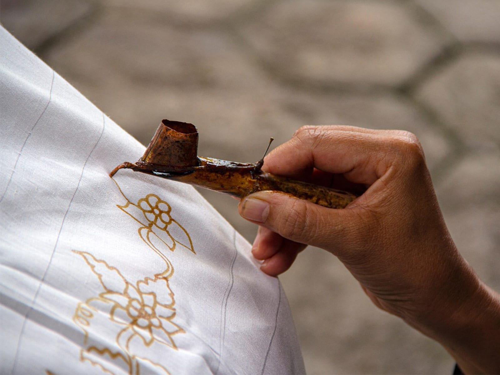 A hand holding a batik tool, drawing intricate designs with wax