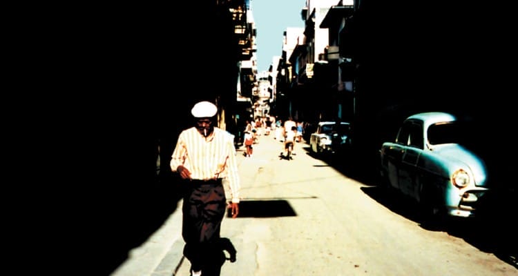 A sepia tone photo of a man wearing dark trousers, white shirt and hat.