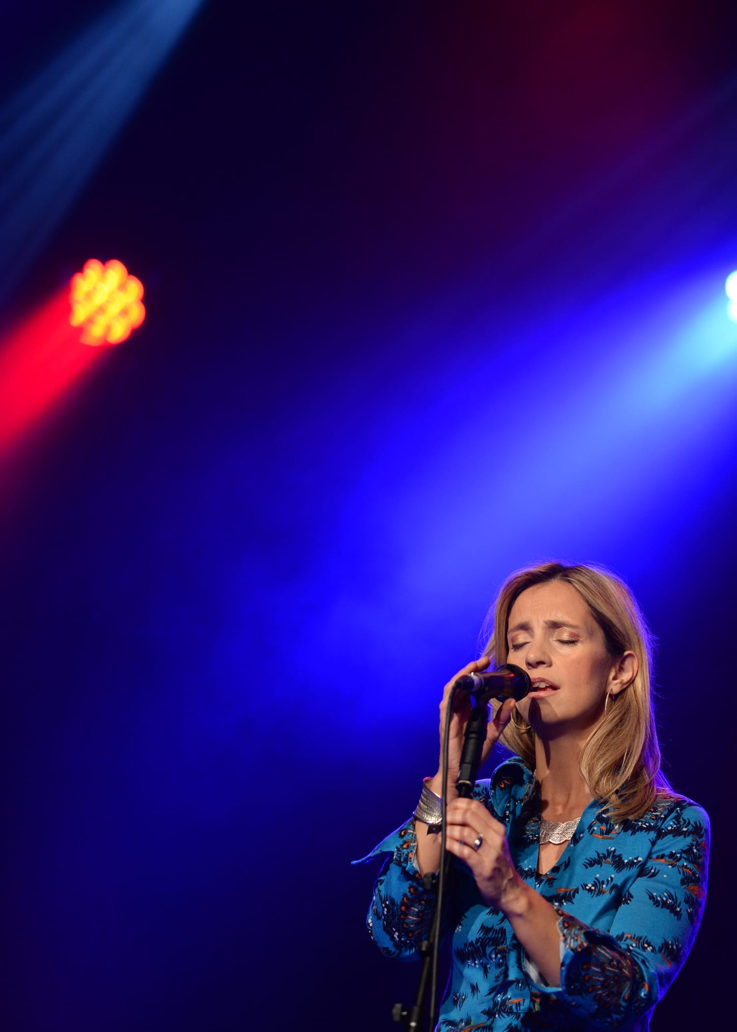 a photo of Cara Dillon singing into a microphone on a stage with blue lights on