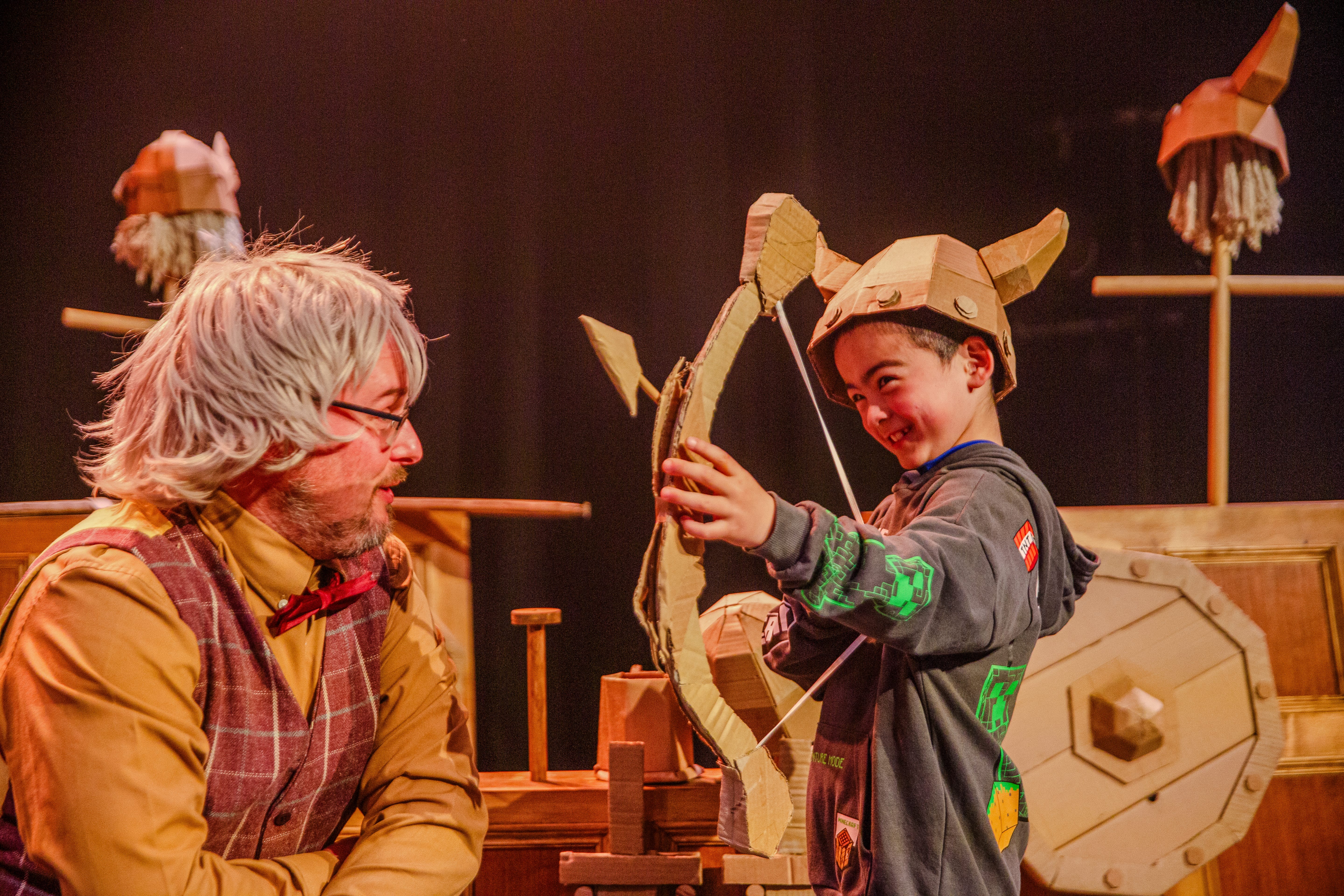 A boy holds a cardboard box and arrow, whilst wearing a cardboard Viking hat.