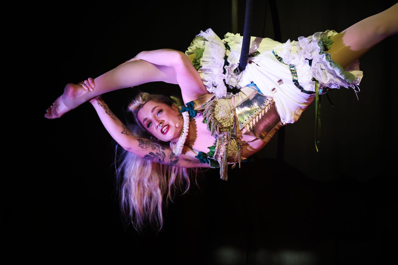 Performer Naomi Woods, a woman with long blond hair, is suspended from the ceiling.