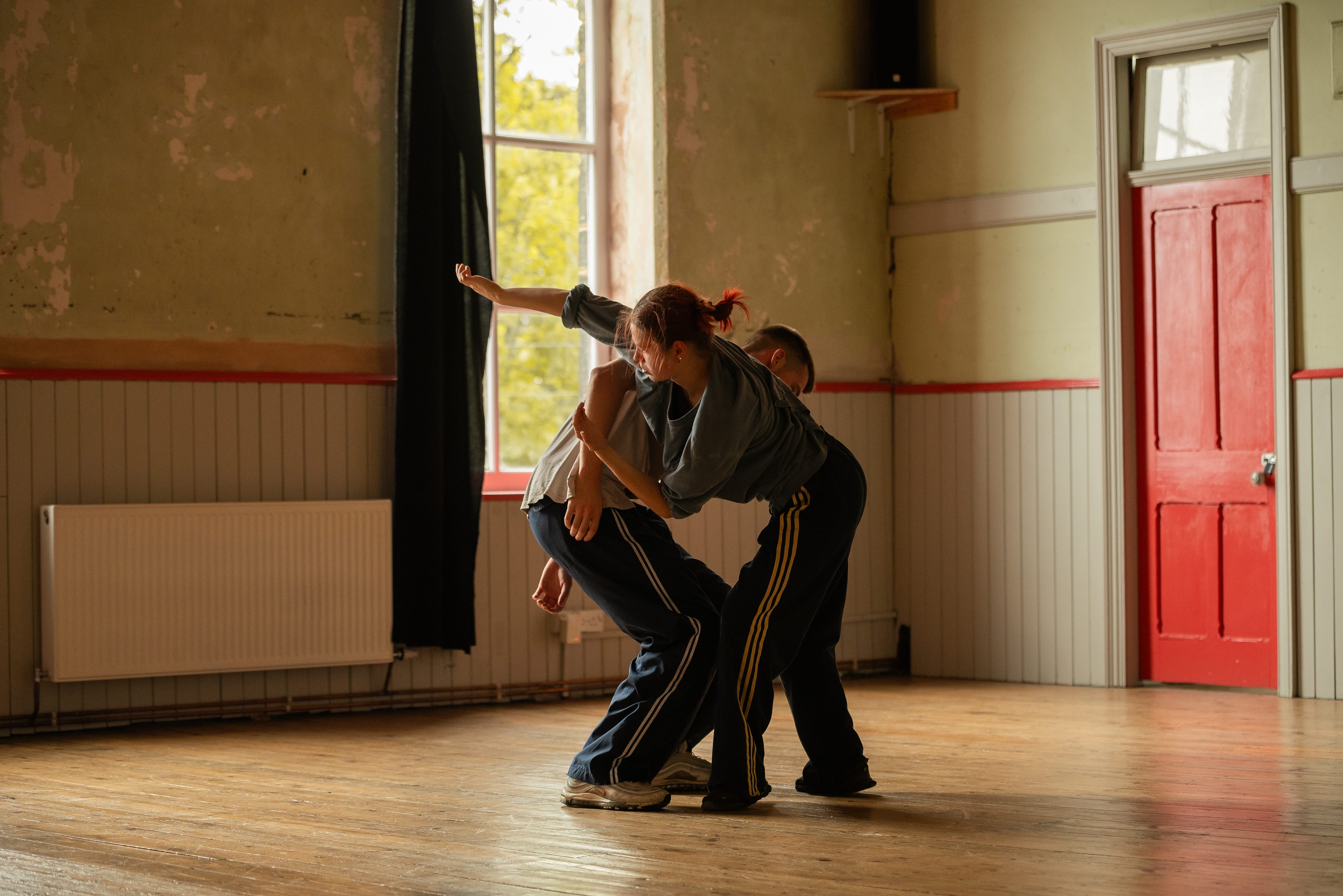 Two dancers rehearse in front of a window.