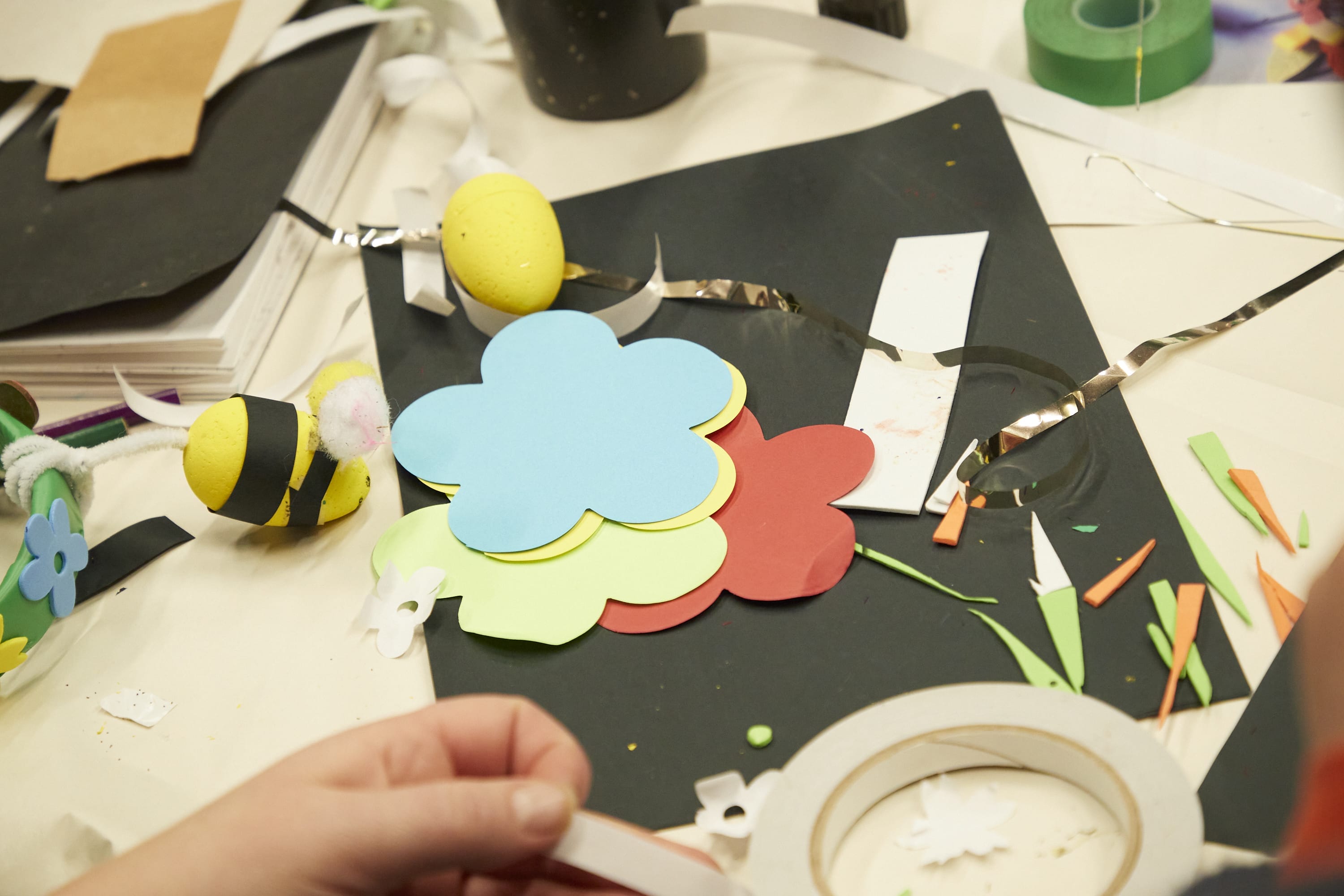 Small hands playing with paper, surrounded by craft supplies.