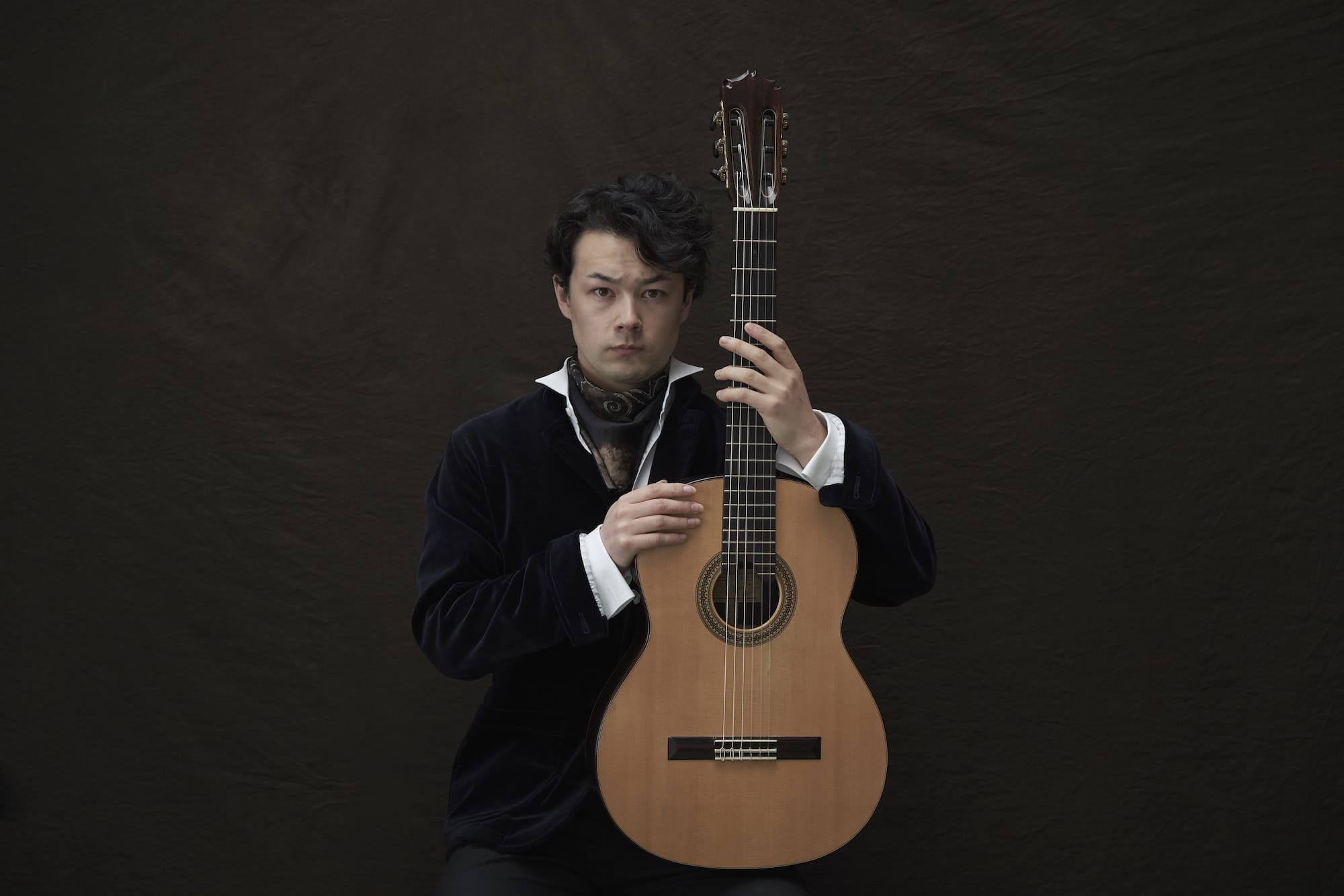 A photo with Sean Shibe holding his guitar with a dark background