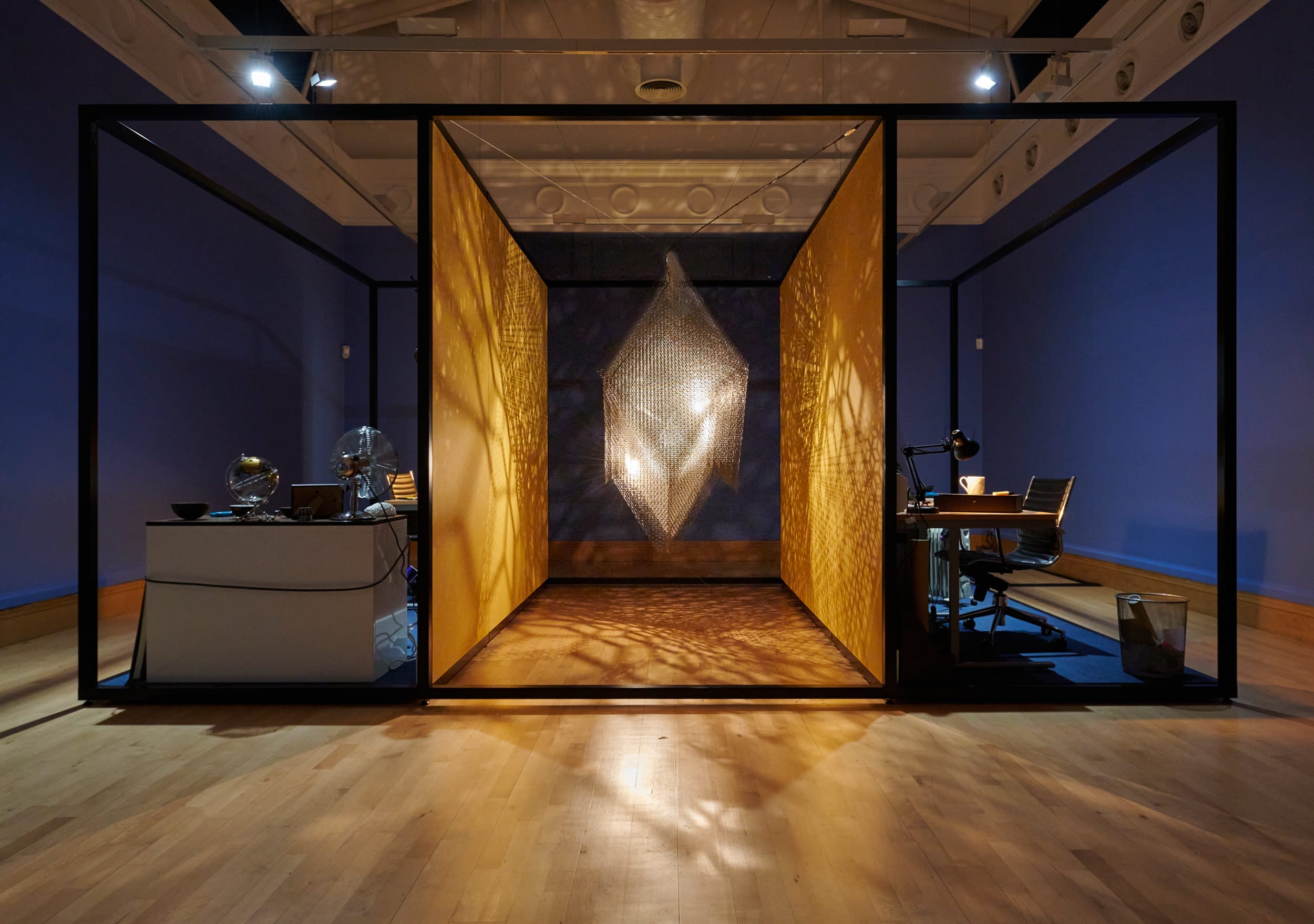 A light cage sits in the middle of a sculpture which features two identical science desks at either side.