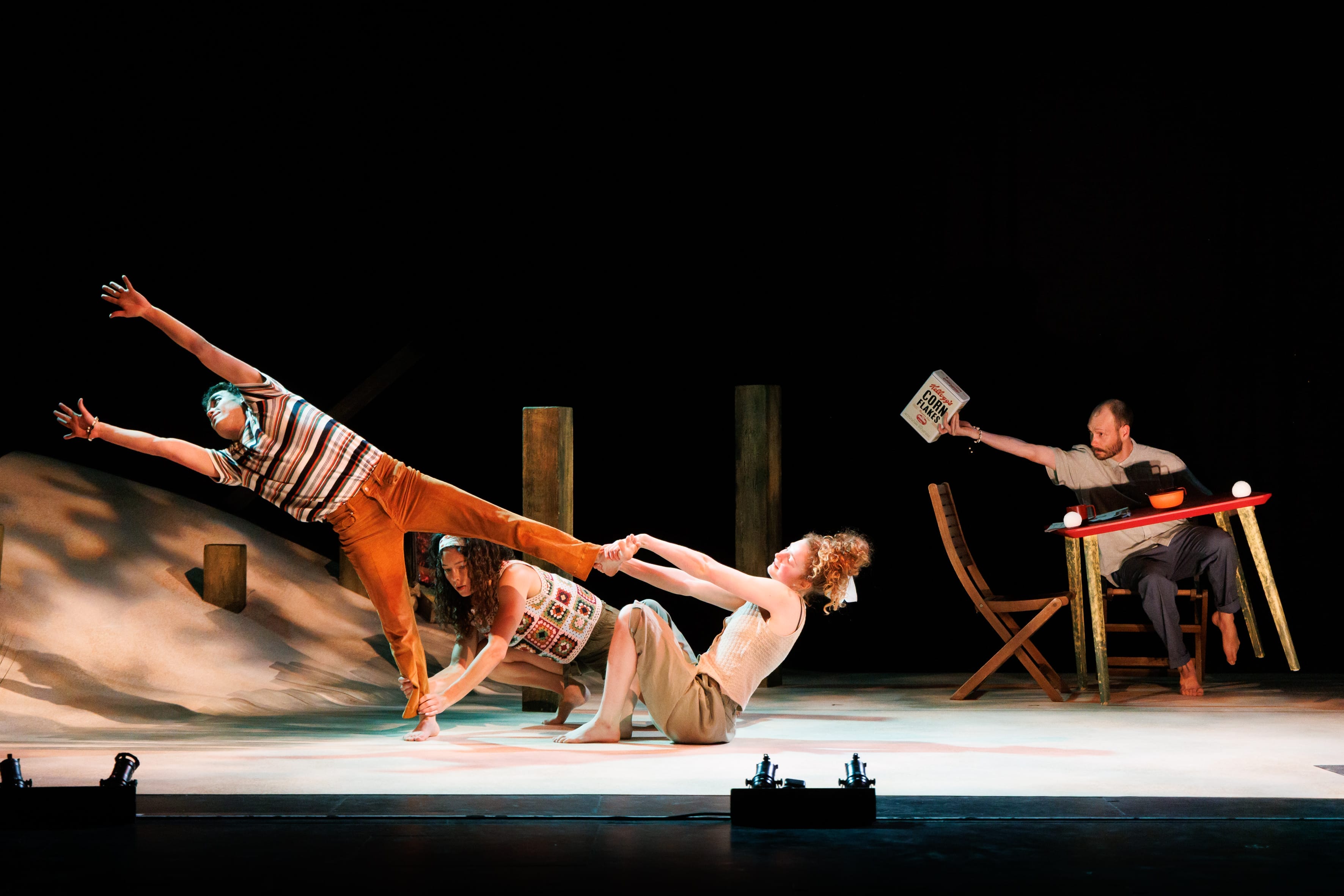 a picture of three people dancing on stage surrounded by sand with two of them holding a third's ankles