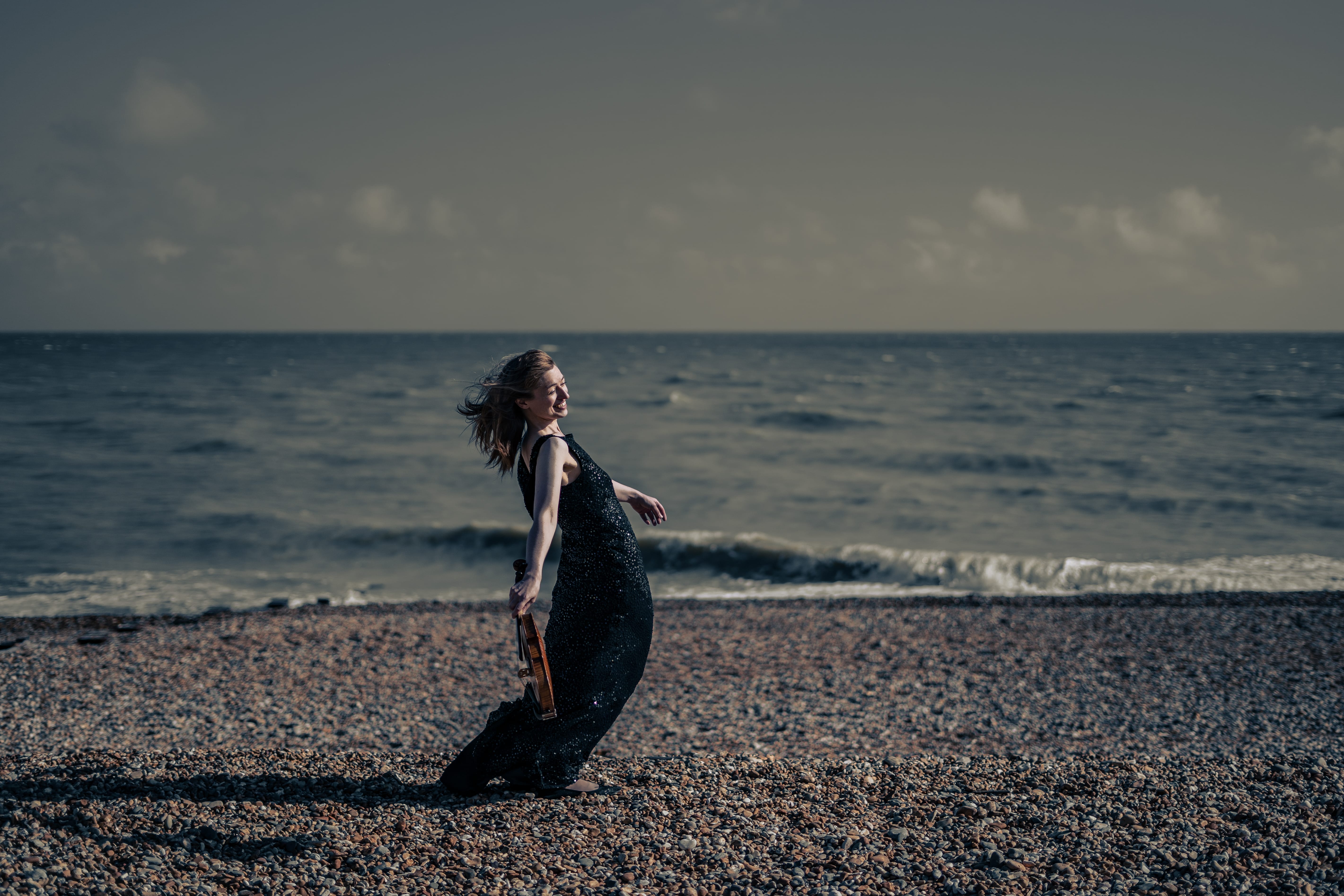 Fenella Humphreys poses gracefully with her violin on a pebble beach