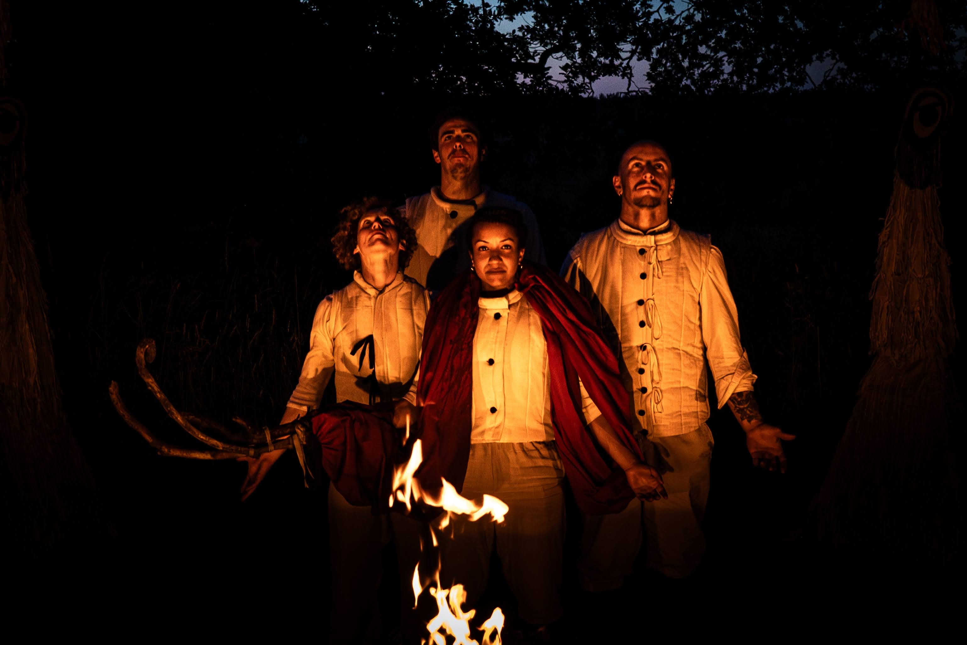 An eerie photo of the people stood around a fire.