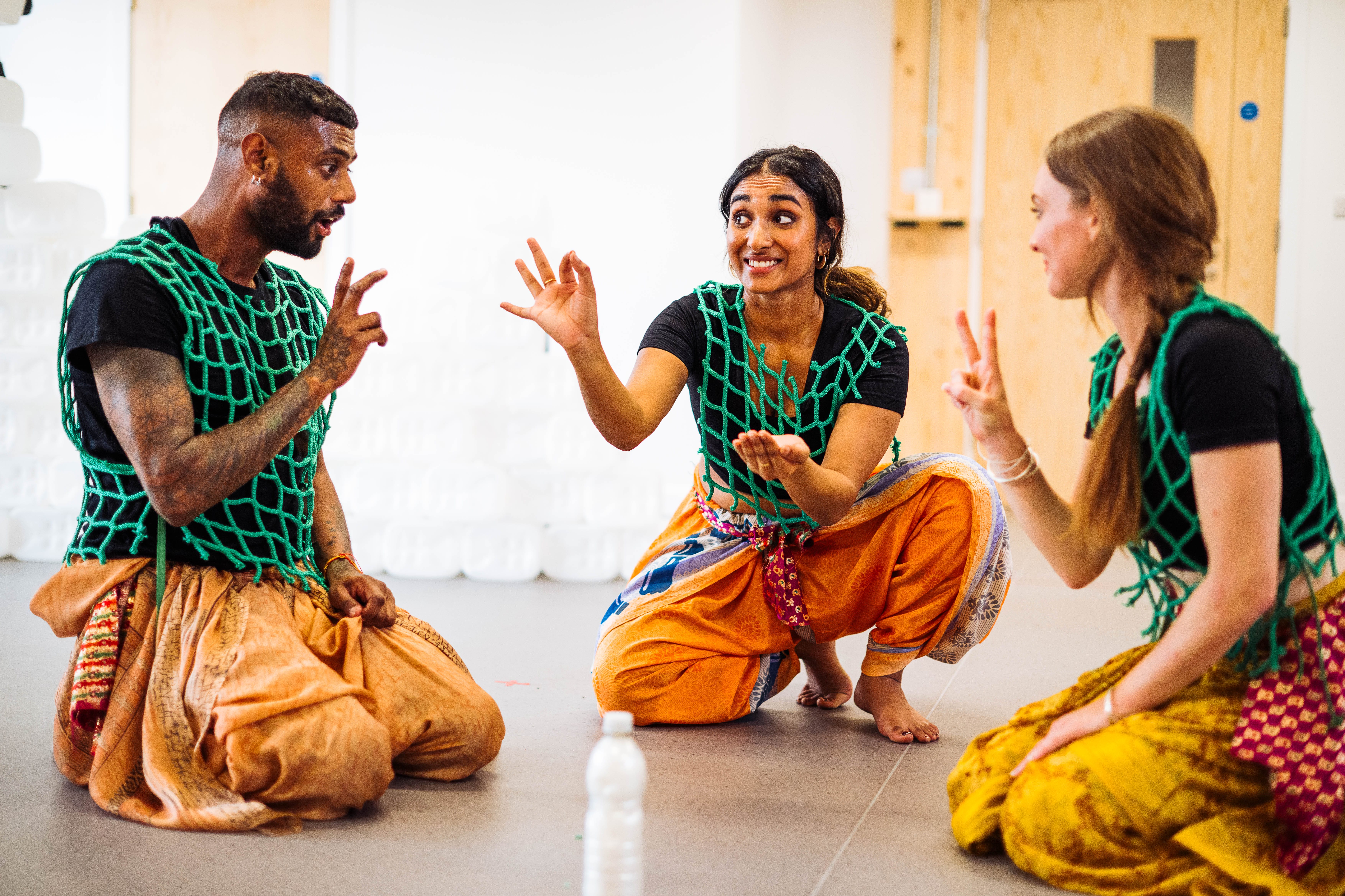 Three performers, wearing fishing net tops, crouch on the floor, counting with their fingers.