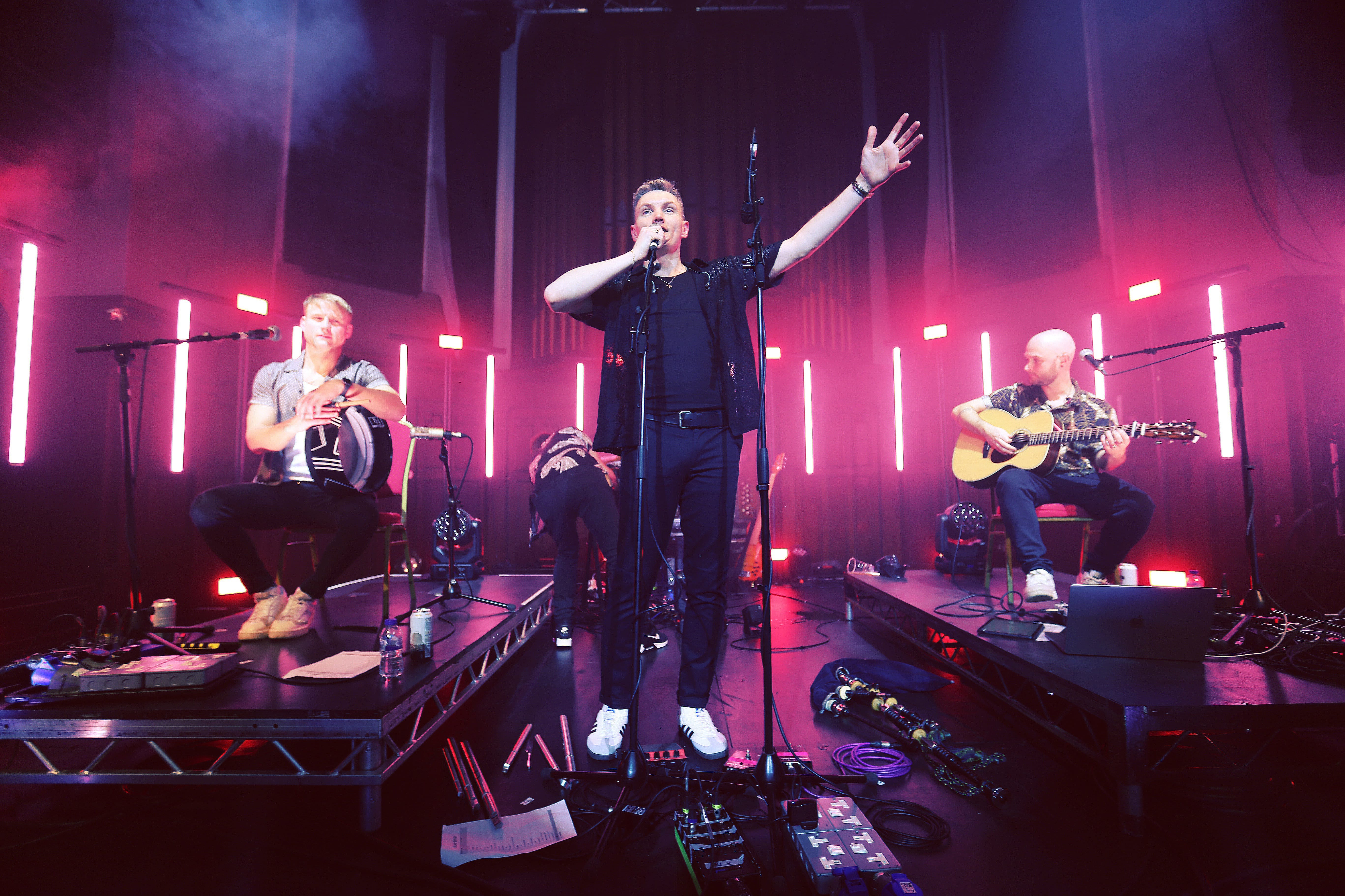 The band Project Smok are dramatically illuminated by neon lights on stage