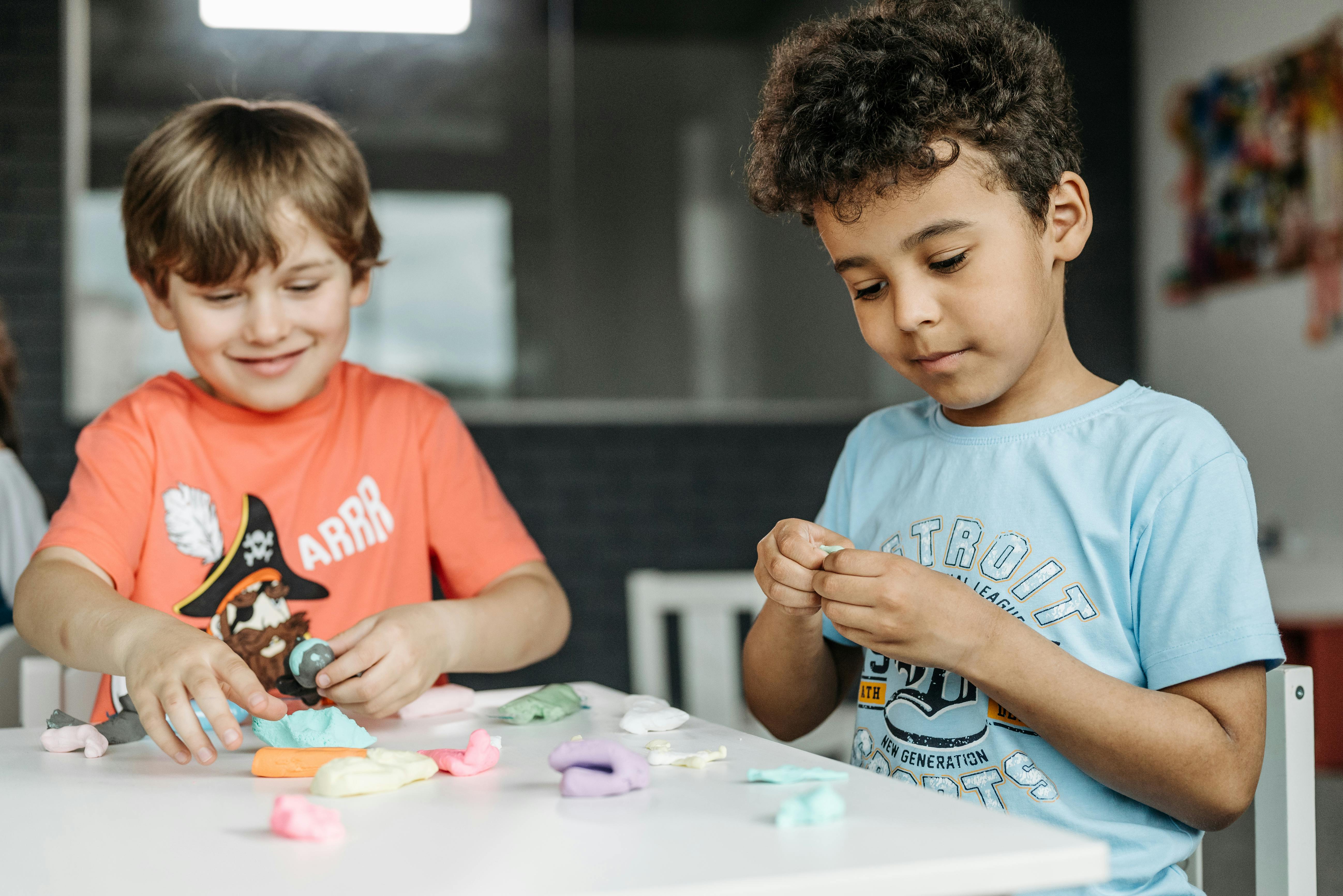 Two small boys sit at a table and play with clay.