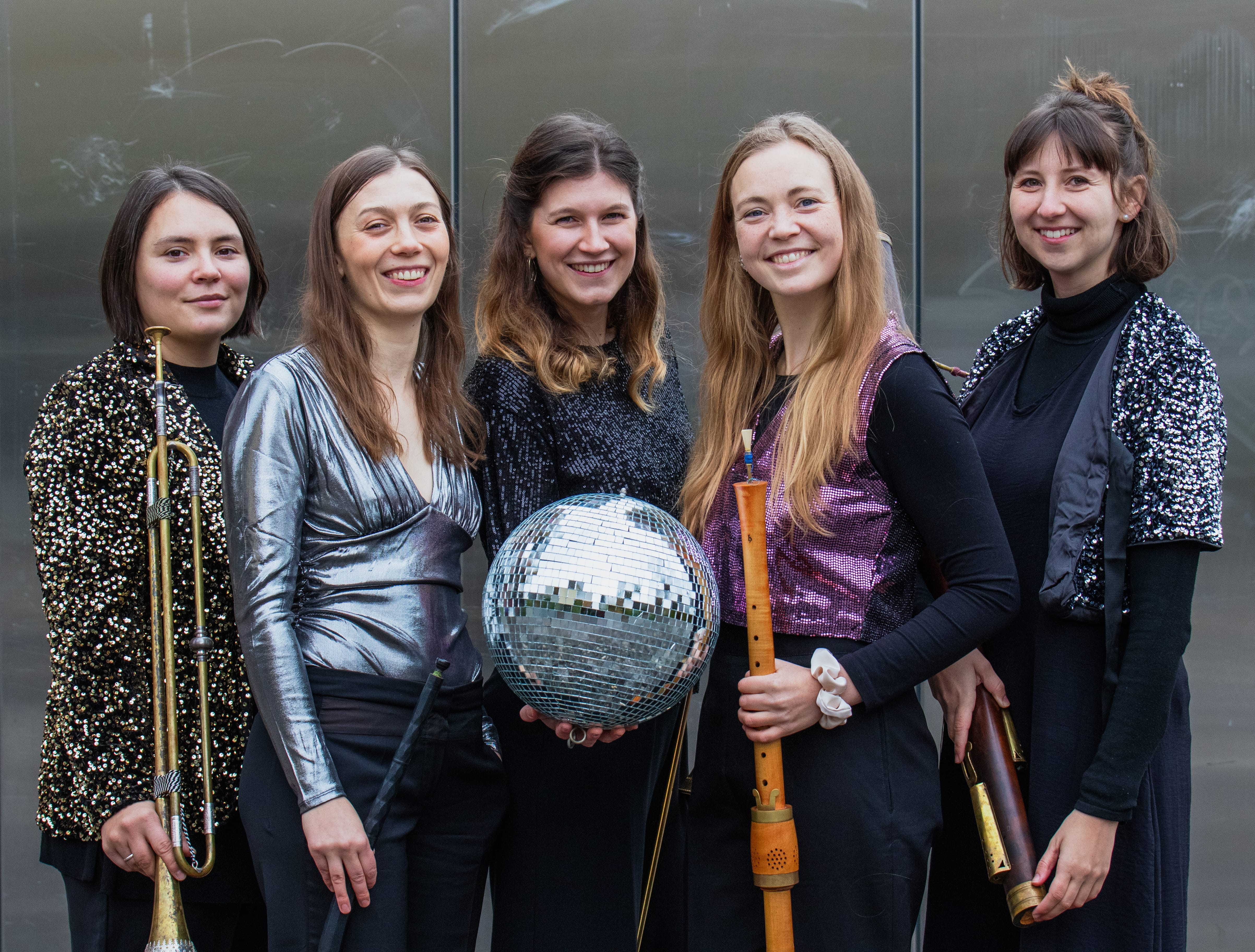 The band smiles enthusiastically at the camera, holding their instruments along with a disco ball.