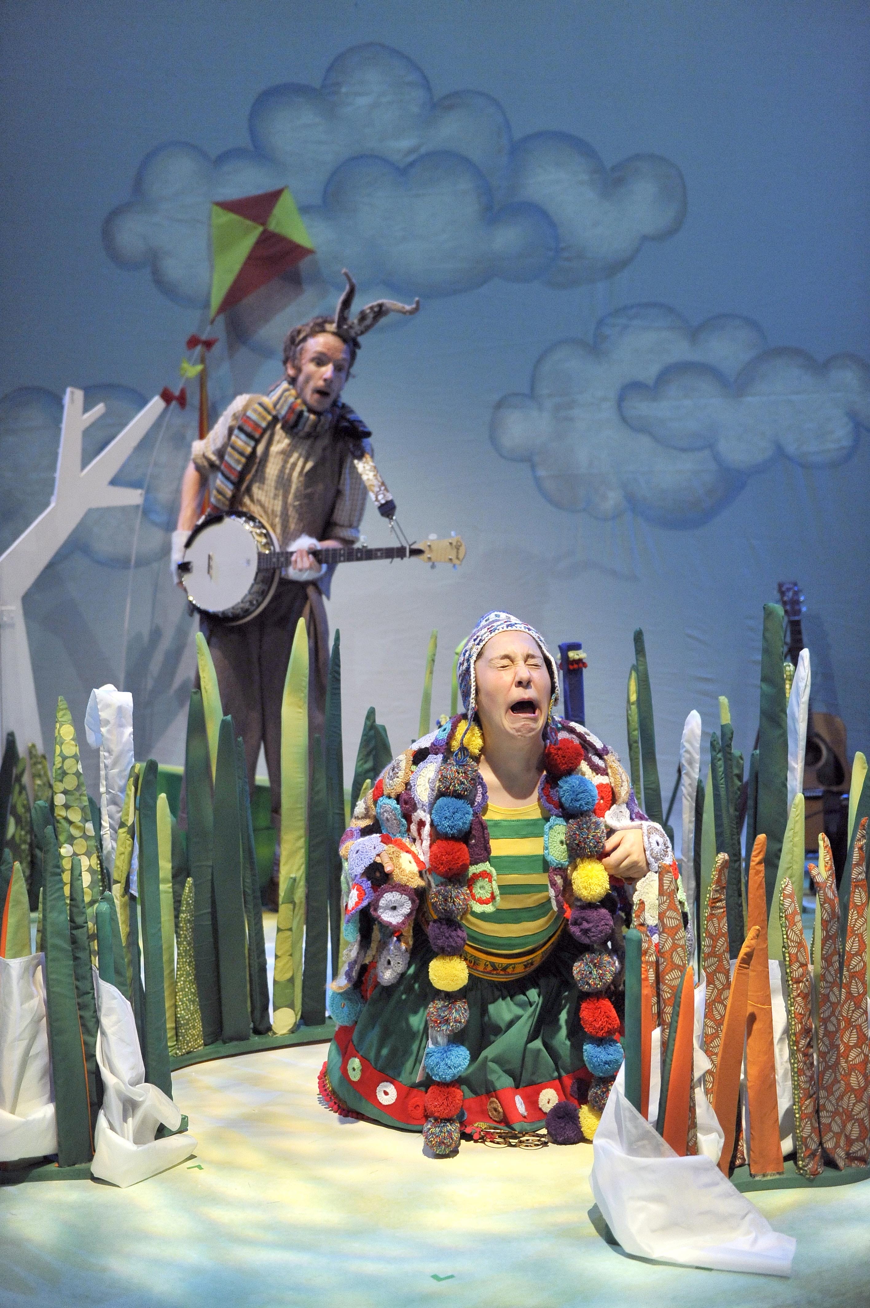 A woman dressed in colourful clothes as a tortoise cries with a man holding an instrument dressed as a hare stands in the background